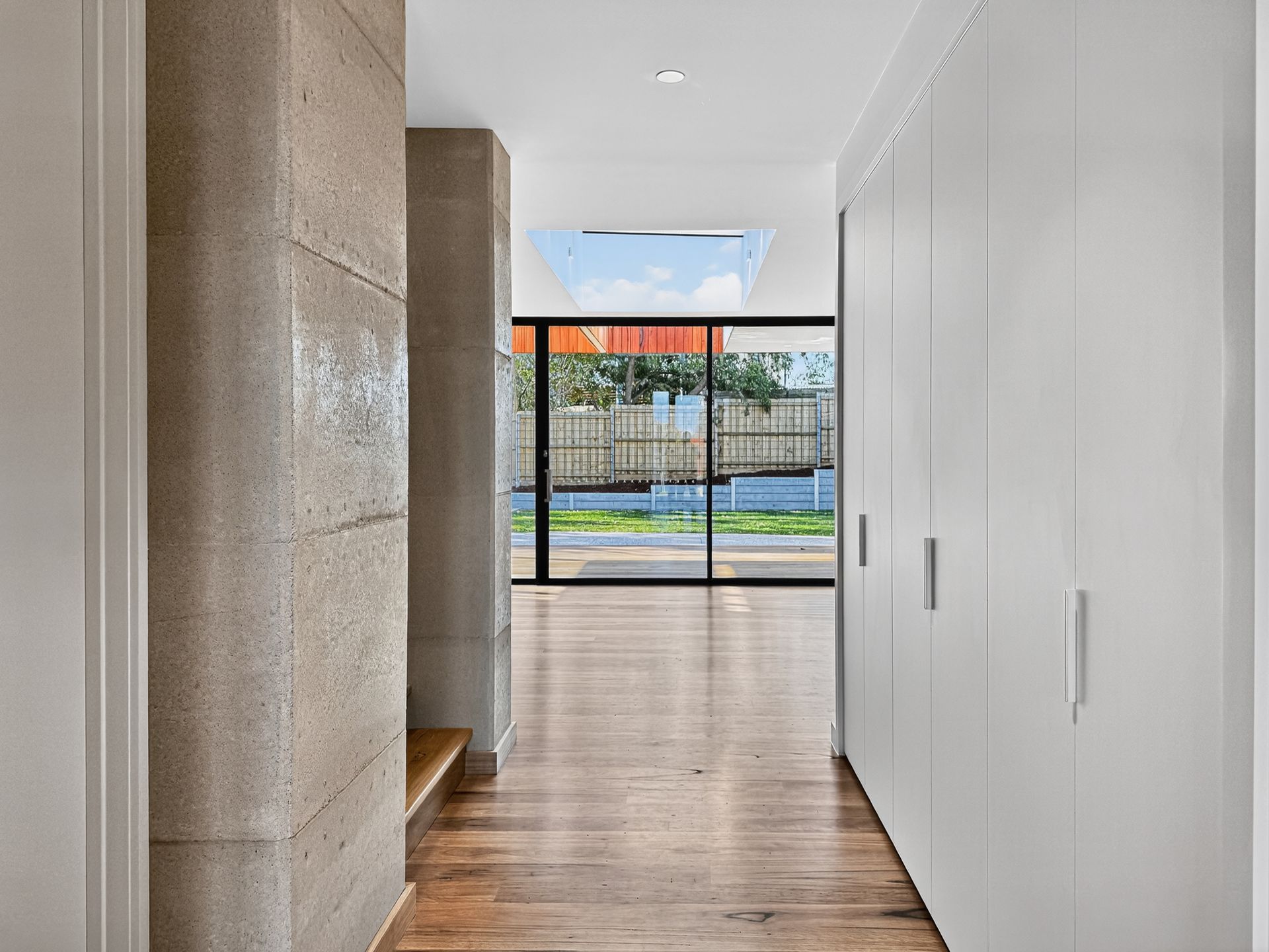 Hallway with wooden floor, white cabinets, and textured concrete pillars leading to a glass door and outdoor view.