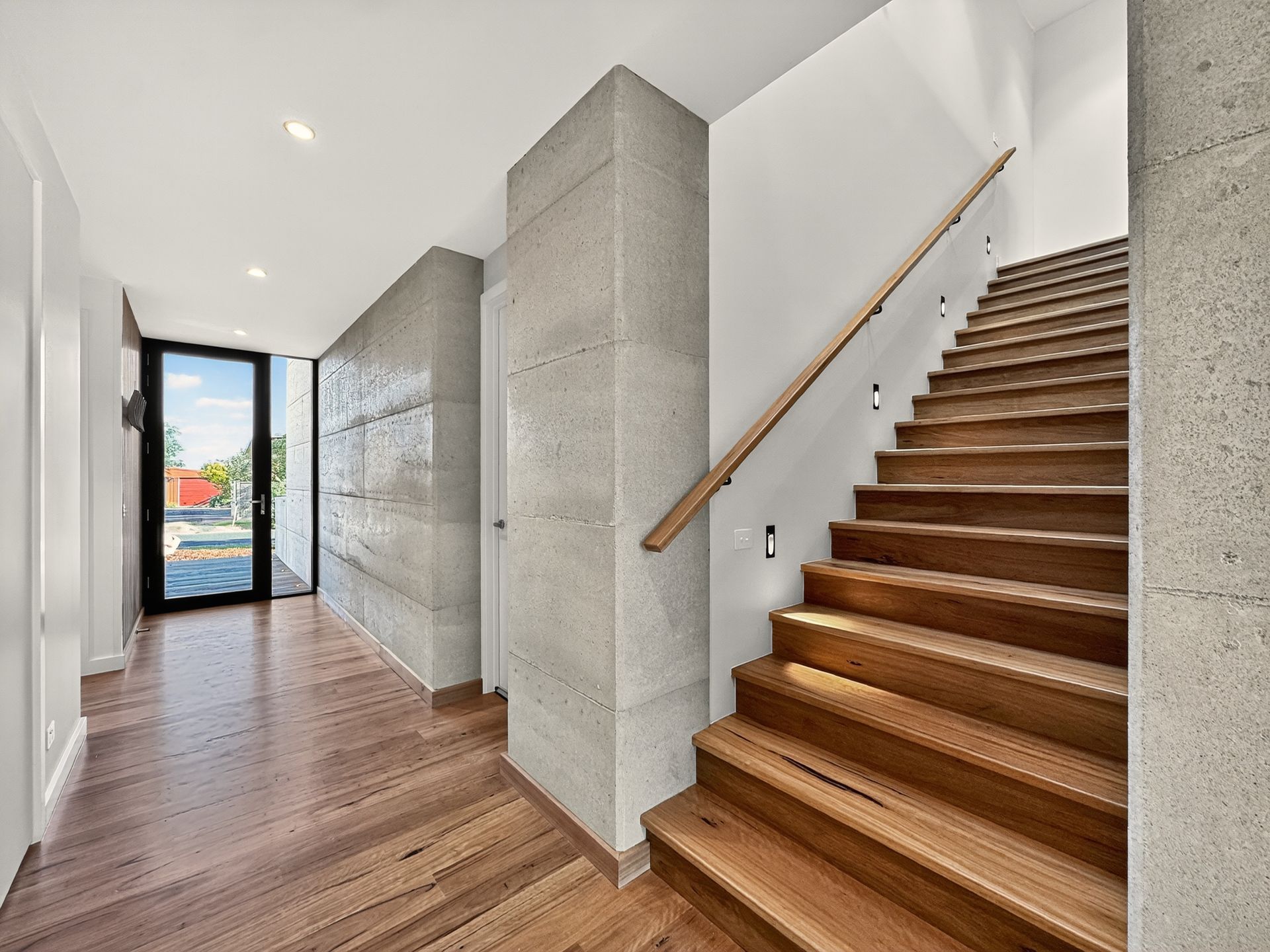 Hallway with wooden stairs, light-colored walls and flooring, and a large door to the left.