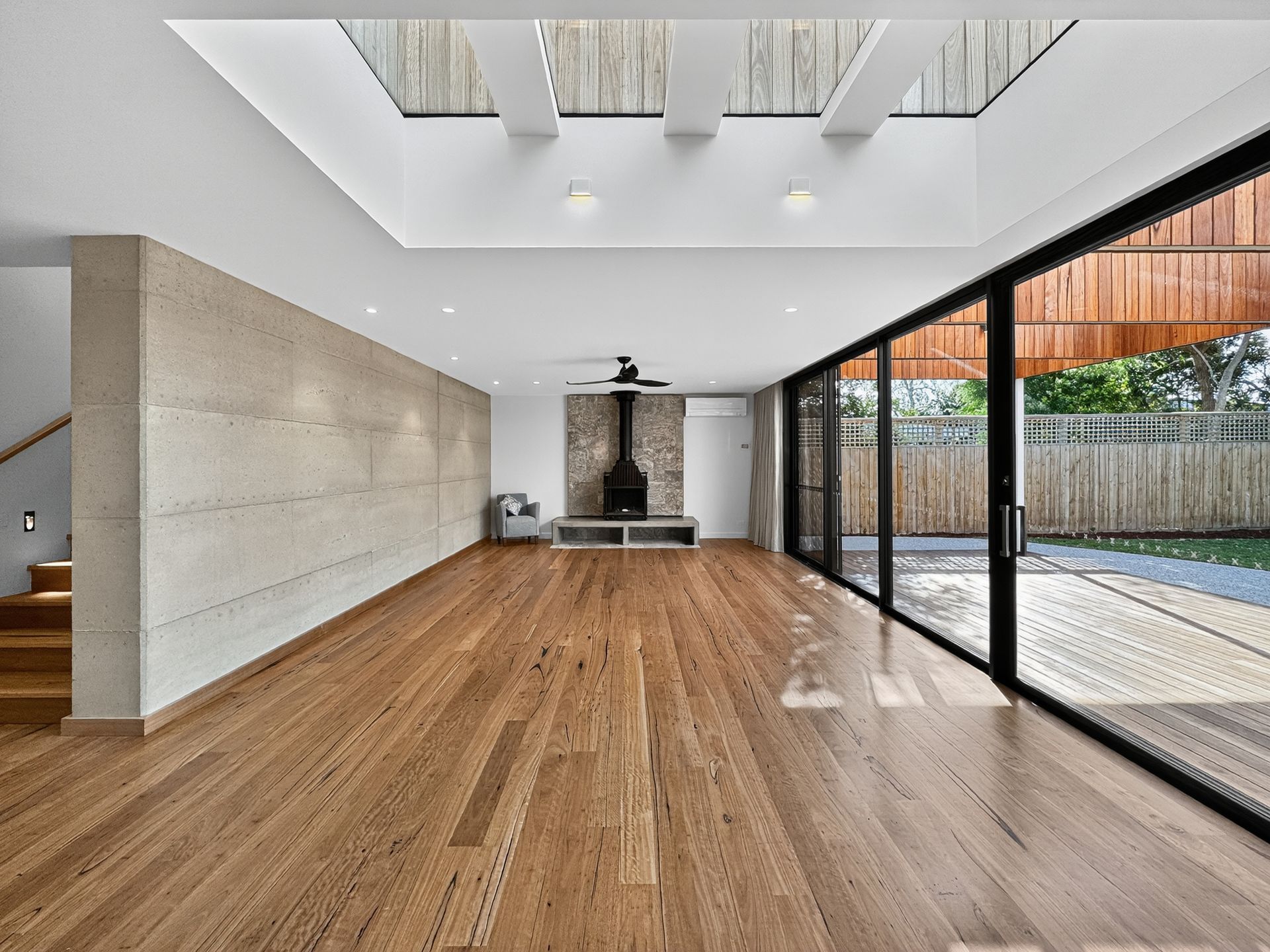 Spacious modern room with wooden floor, sliding glass doors, and skylights. A fireplace is centered on the back wall.