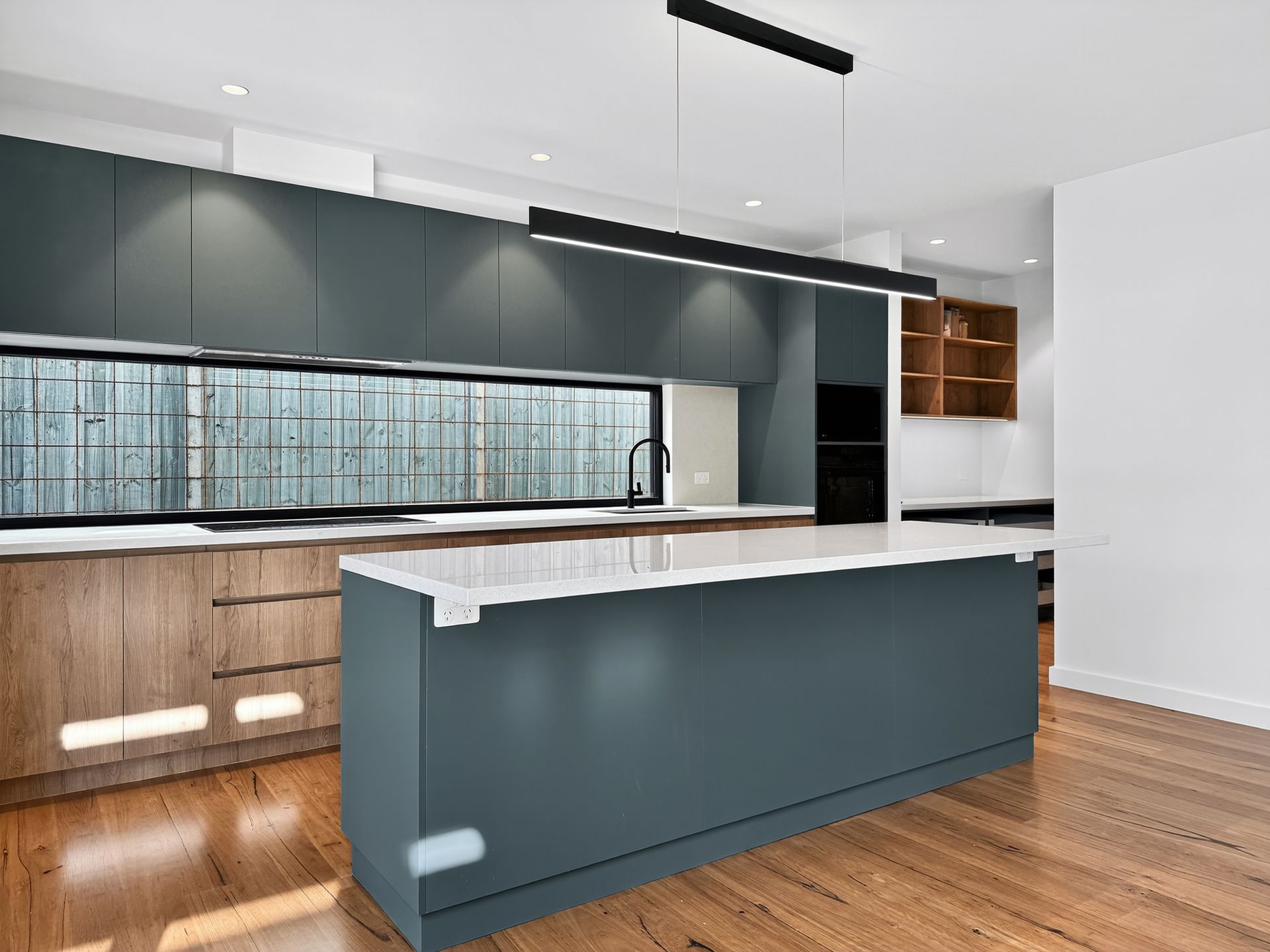 Modern kitchen with teal cabinetry, wood accents, and a large window.