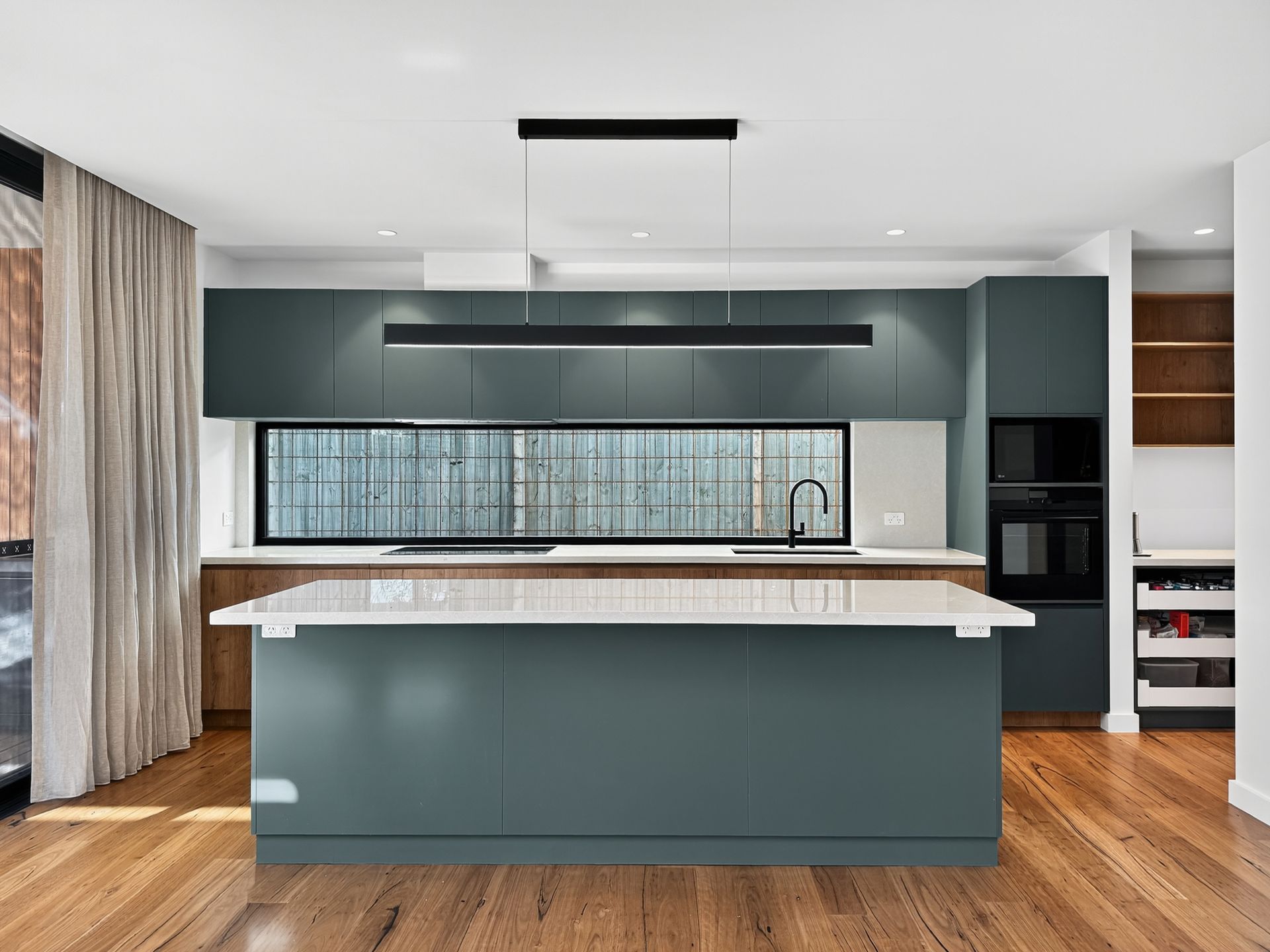 Modern kitchen with teal cabinets, large island, and wood flooring.