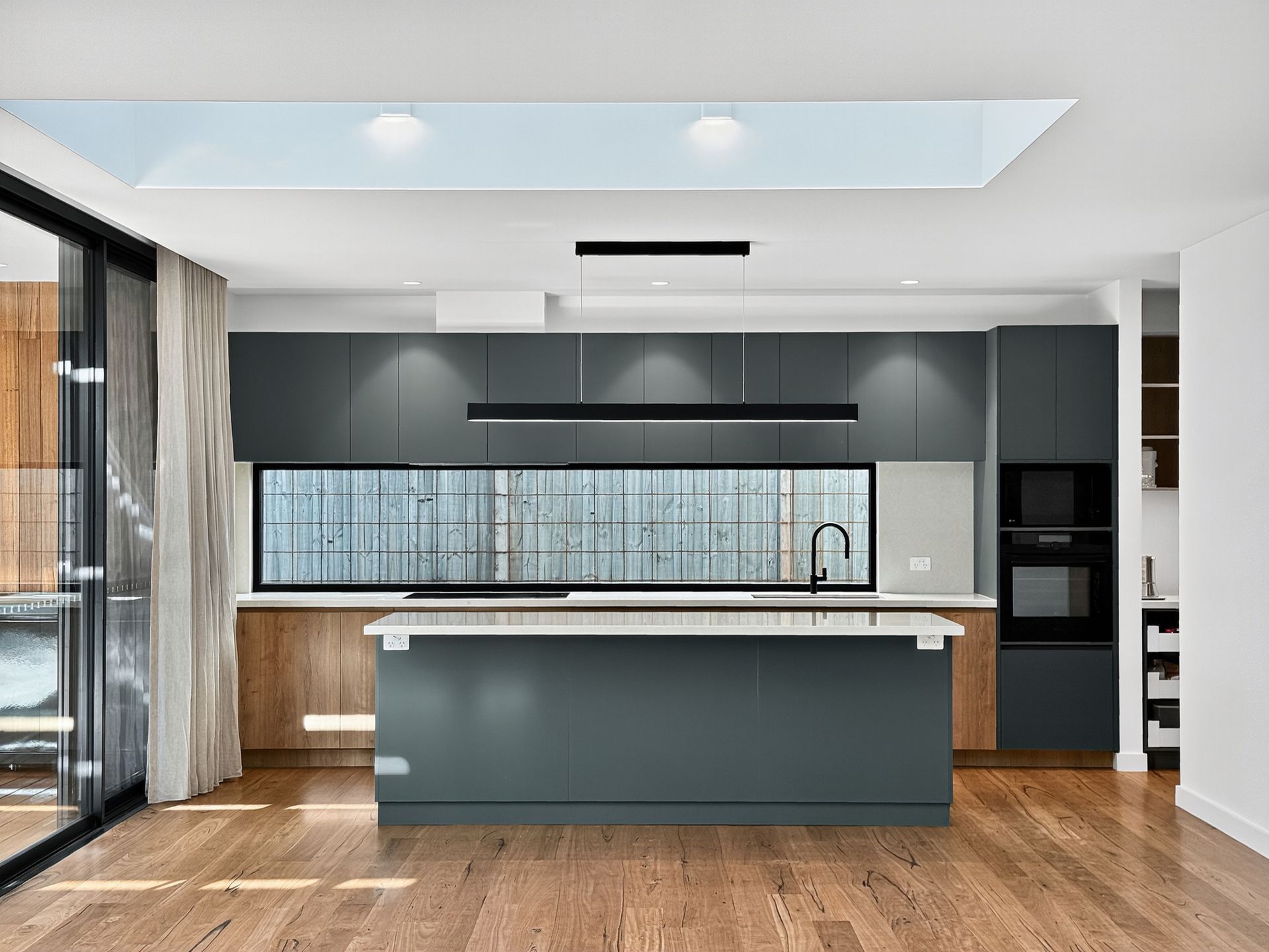 Modern kitchen with gray cabinets, wood floors, and island. Natural light floods the space from a skylight.