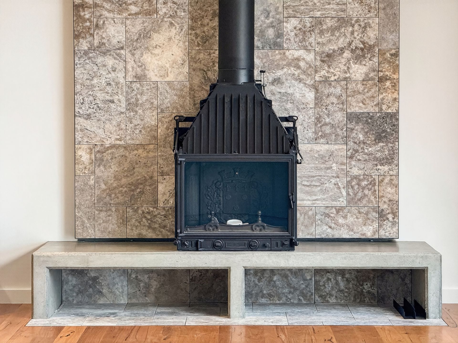 Fireplace with a black metal insert and chimney against a stone-tiled wall, atop a concrete hearth.