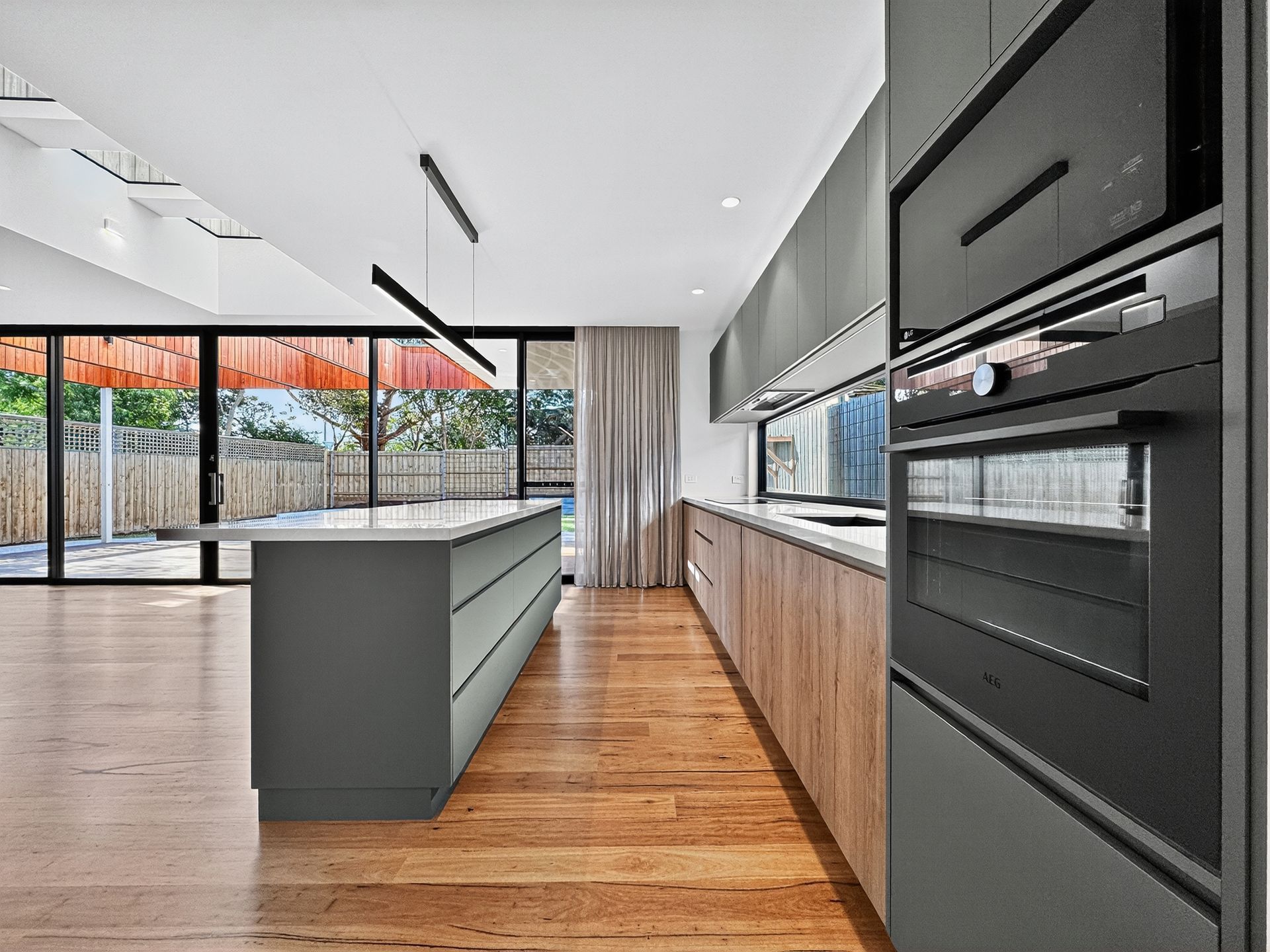 Modern kitchen with wooden floors, island, and dark gray cabinets, overlooking a patio.