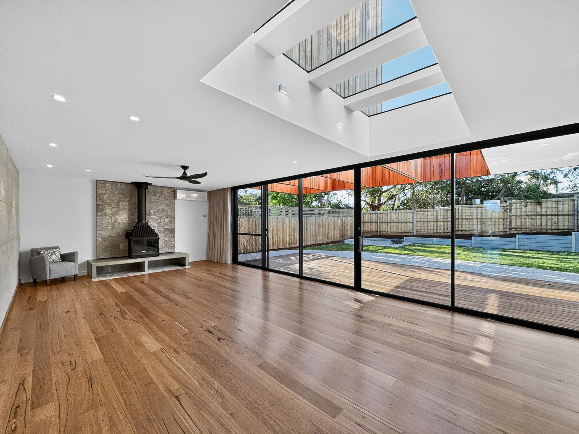 Spacious living room with wood floors, large windows, skylight, and stone fireplace.