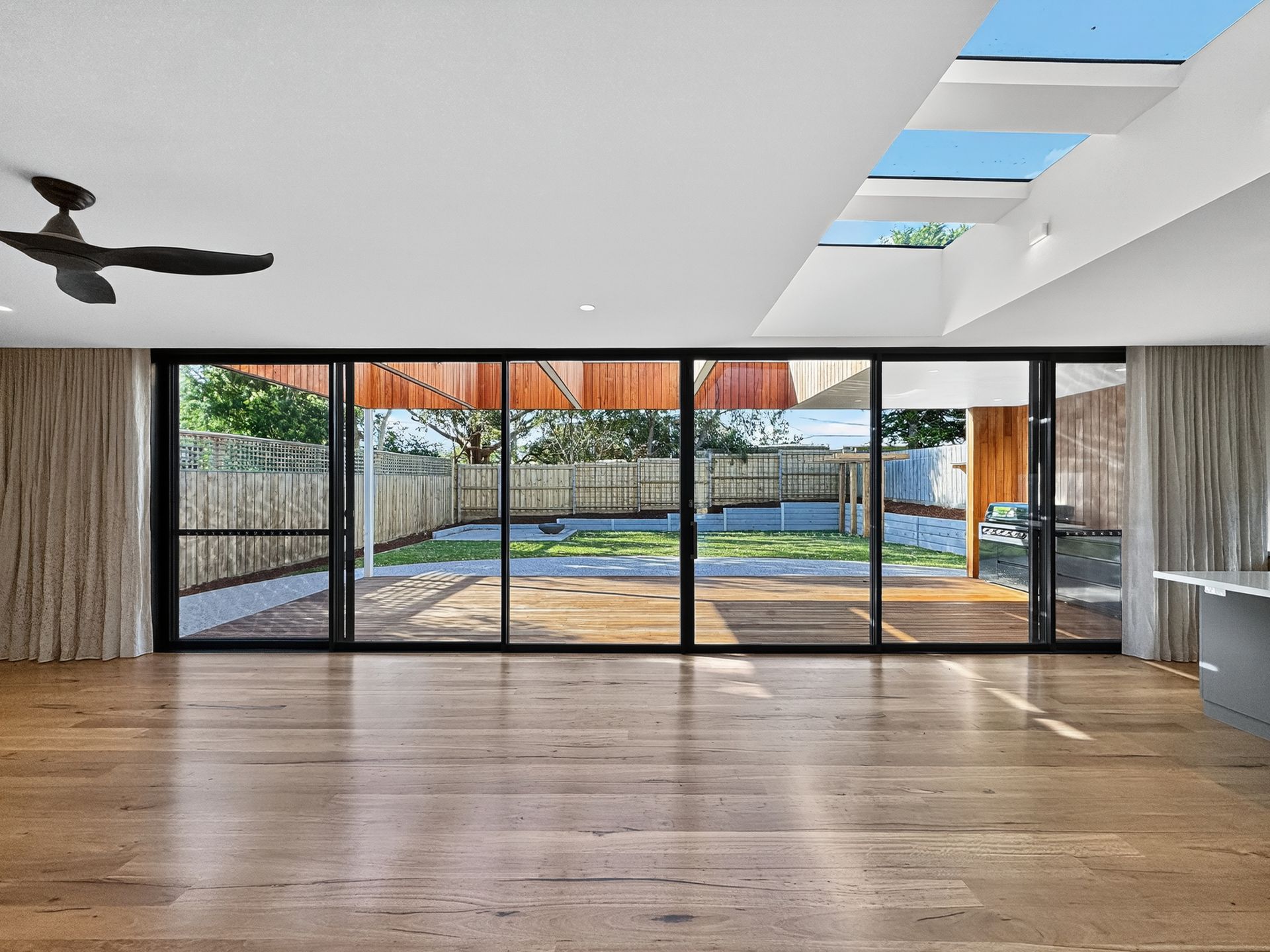 Spacious room with large glass doors opening to a backyard, skylights above, and a ceiling fan.