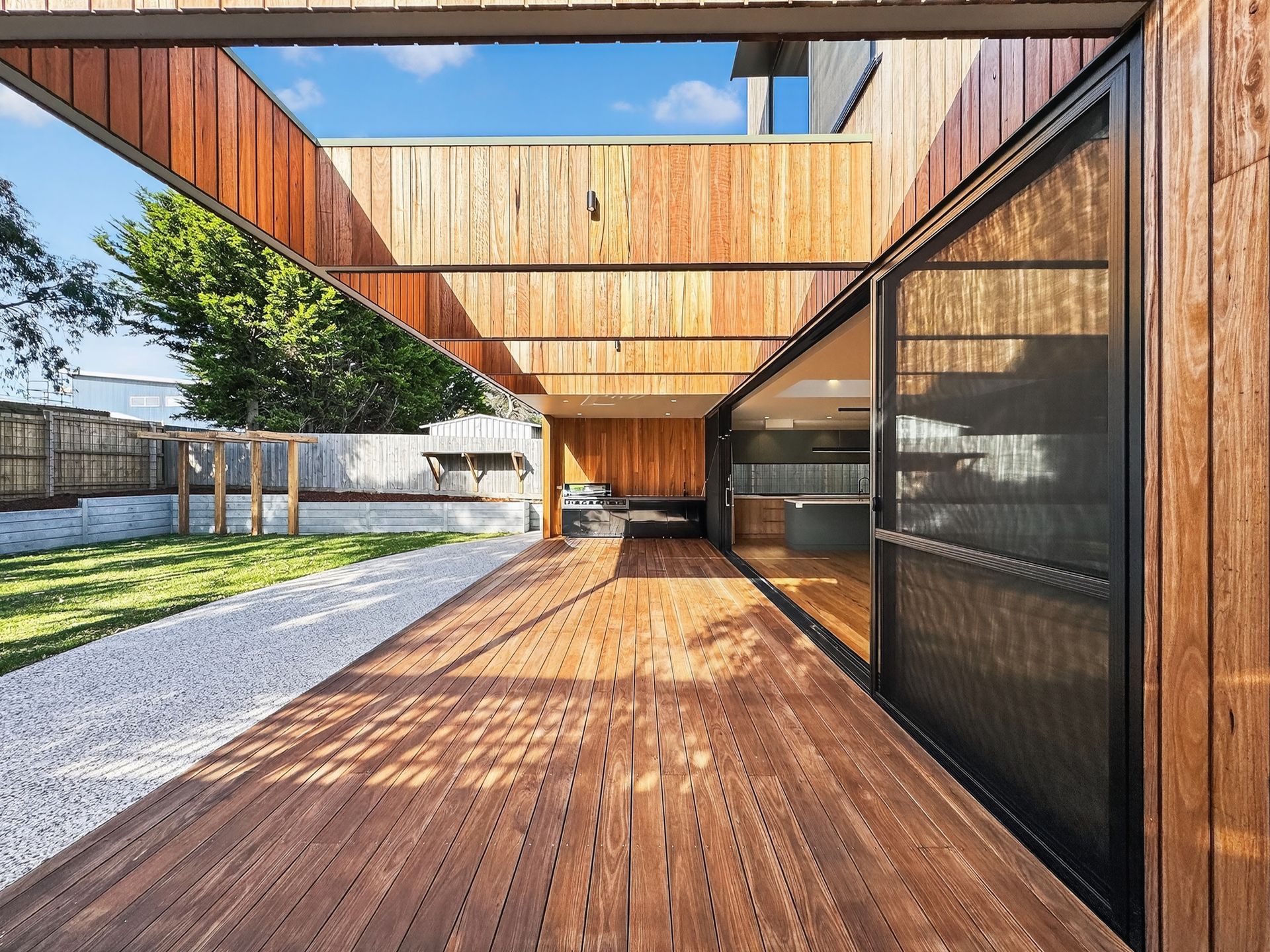 Wooden deck with pergola, leads to glass sliding doors and backyard.