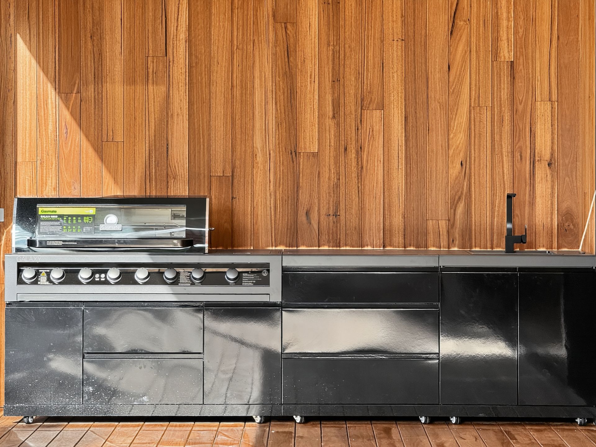 Outdoor black grilling kitchen with a stainless steel grill against wood paneling.