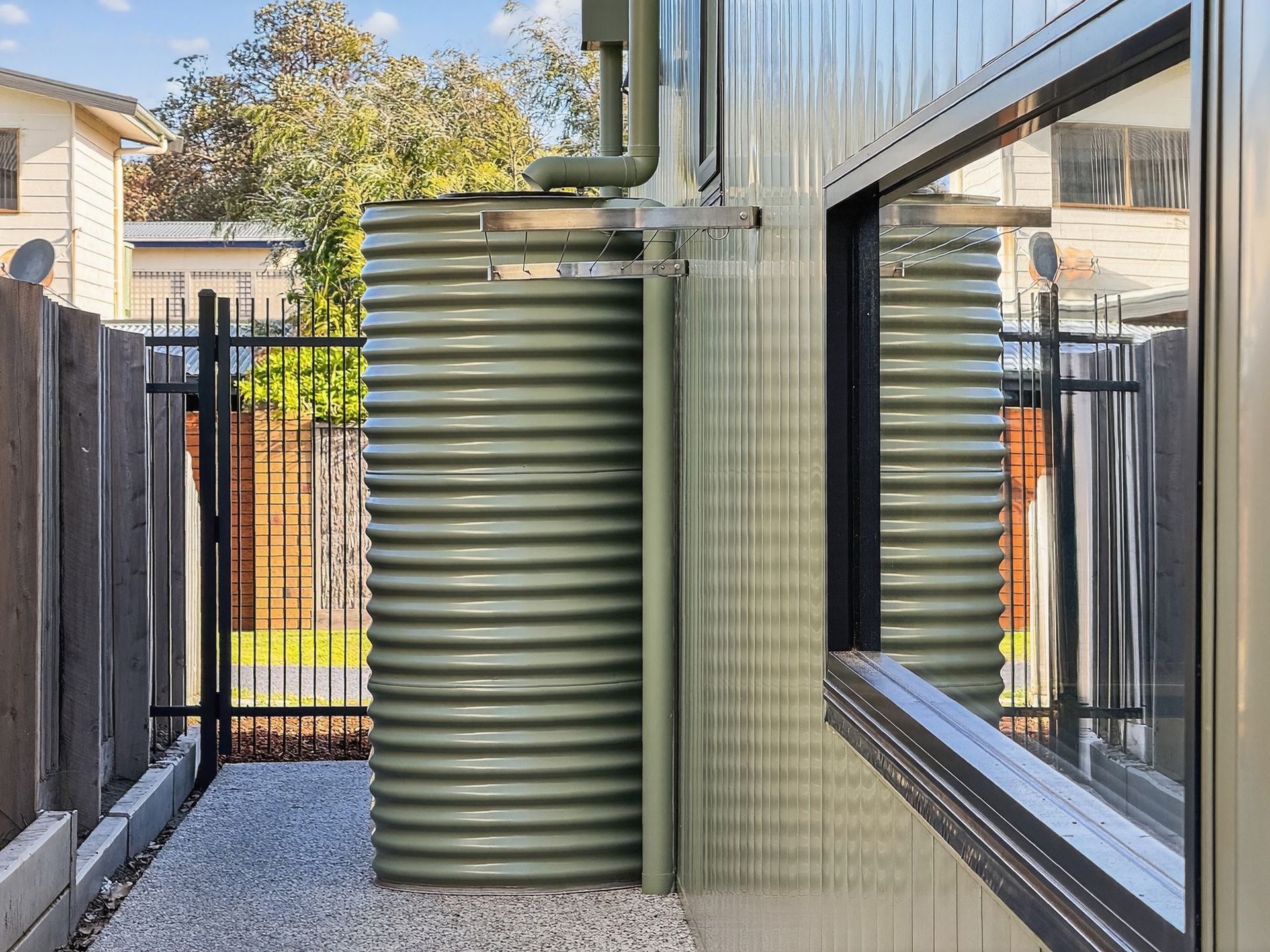 Green corrugated water tank next to a building, with window and fence.