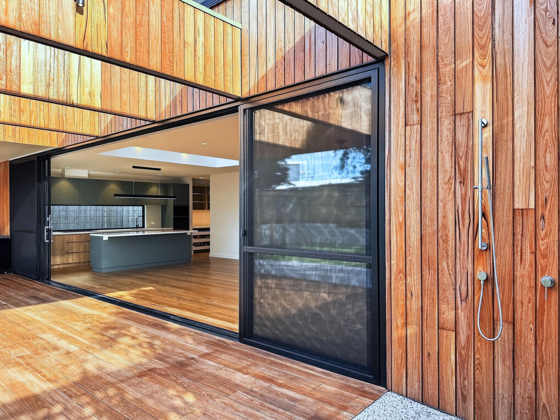 Wooden home exterior with sliding glass doors open to kitchen and an outdoor shower.