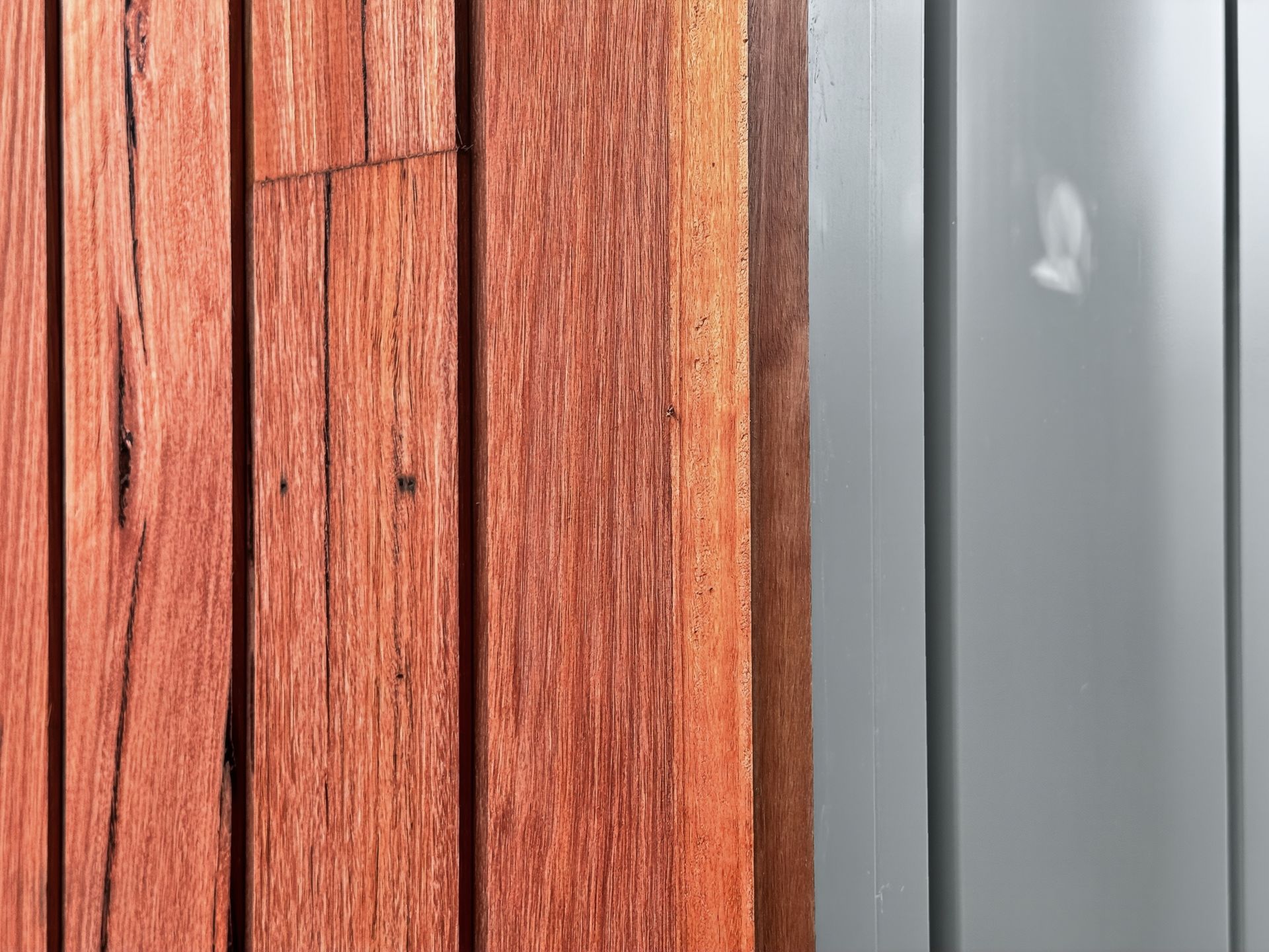 Close-up of reddish-brown wooden planks next to a section of vertical, light-gray siding.