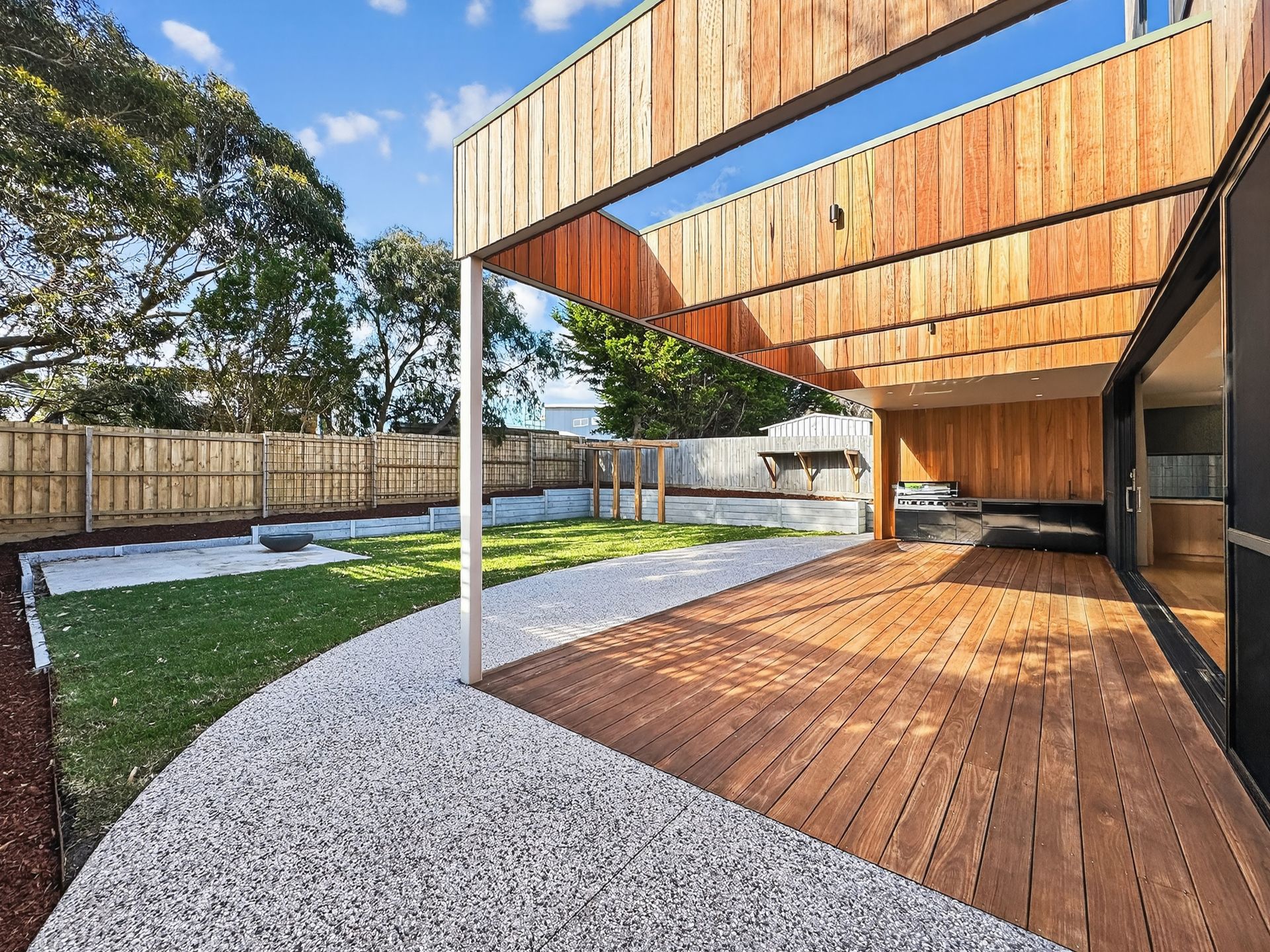 Wooden deck and exterior of house with slatted wood details, overlooking a grassy yard with gravel border.