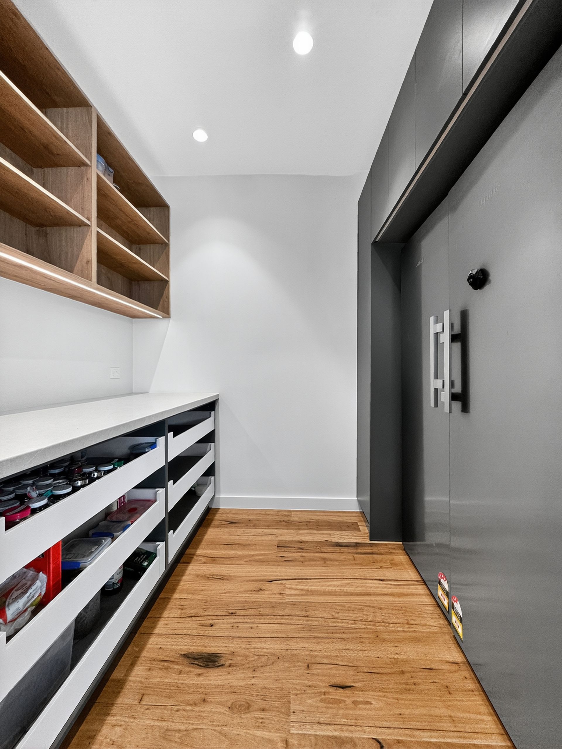 Narrow hallway with wood floor, shelves and white countertop, and gray door.