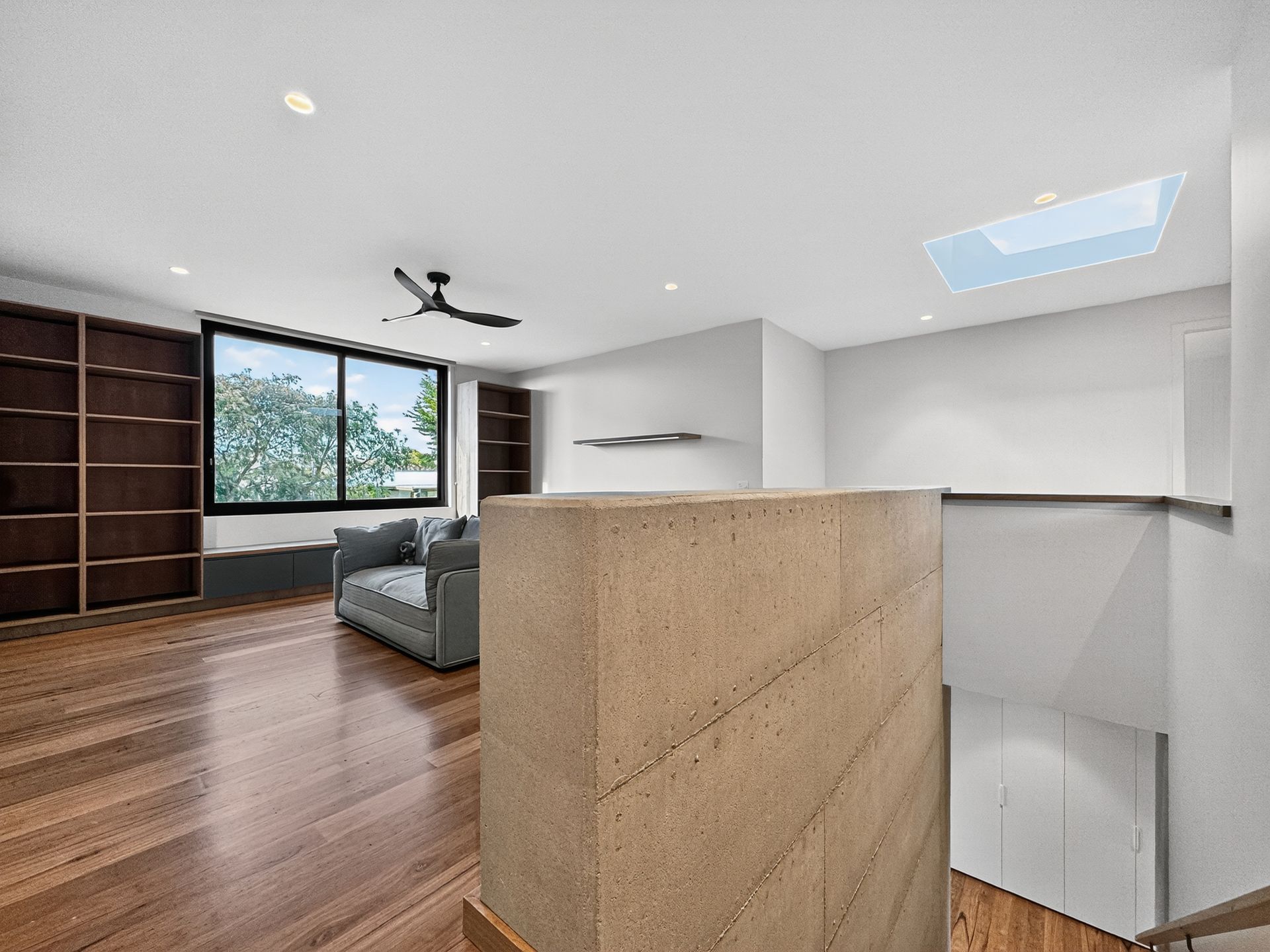 A modern living room with hardwood floors, built-in bookshelves, and large window overlooking trees.