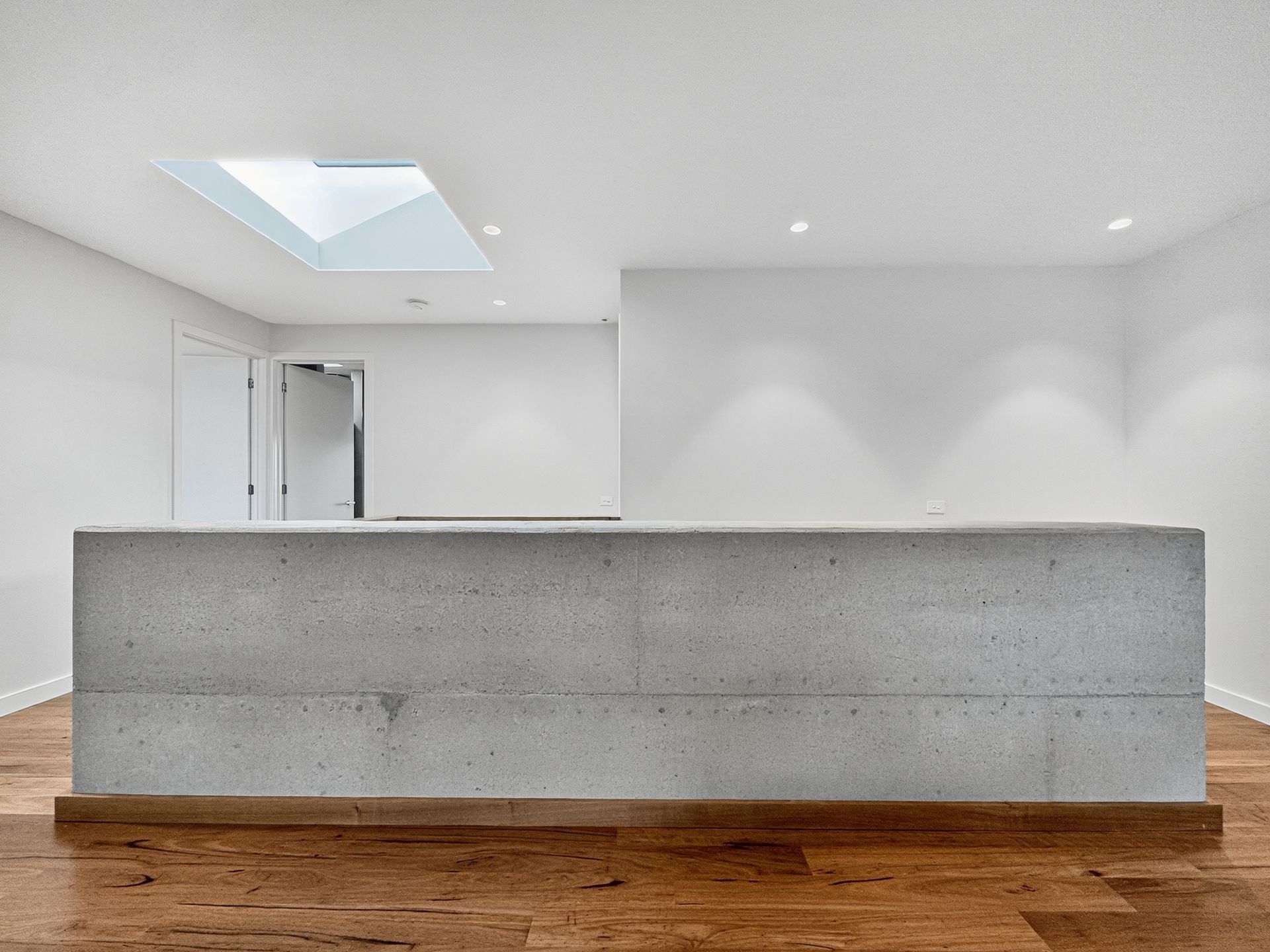 Concrete barrier on wood floor in white room with skylight and door.
