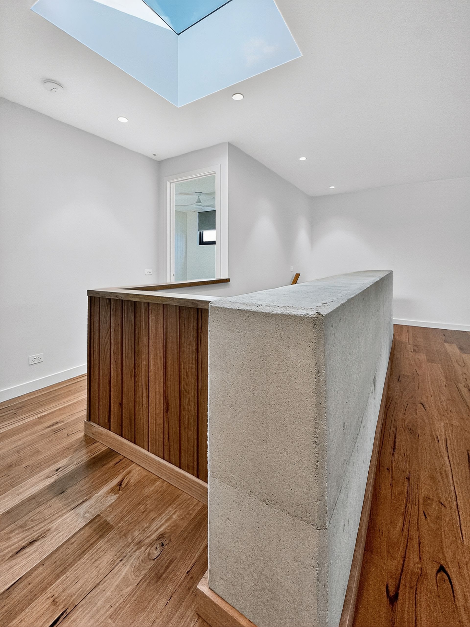 Interior view of a modern landing with wood and concrete railing. Skylight overhead, hardwood floors, and white walls.