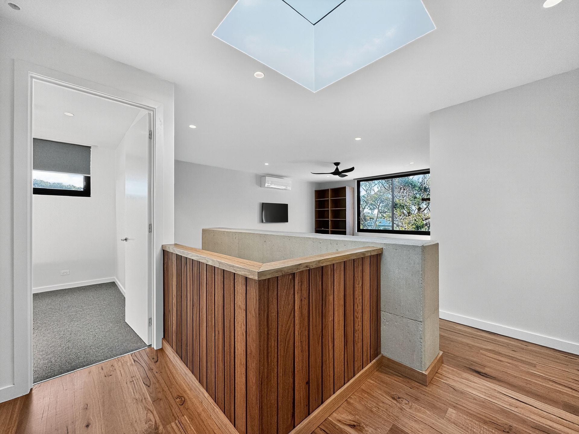 Hallway with wooden railing, skylight, and doorway leading to a room with a window.