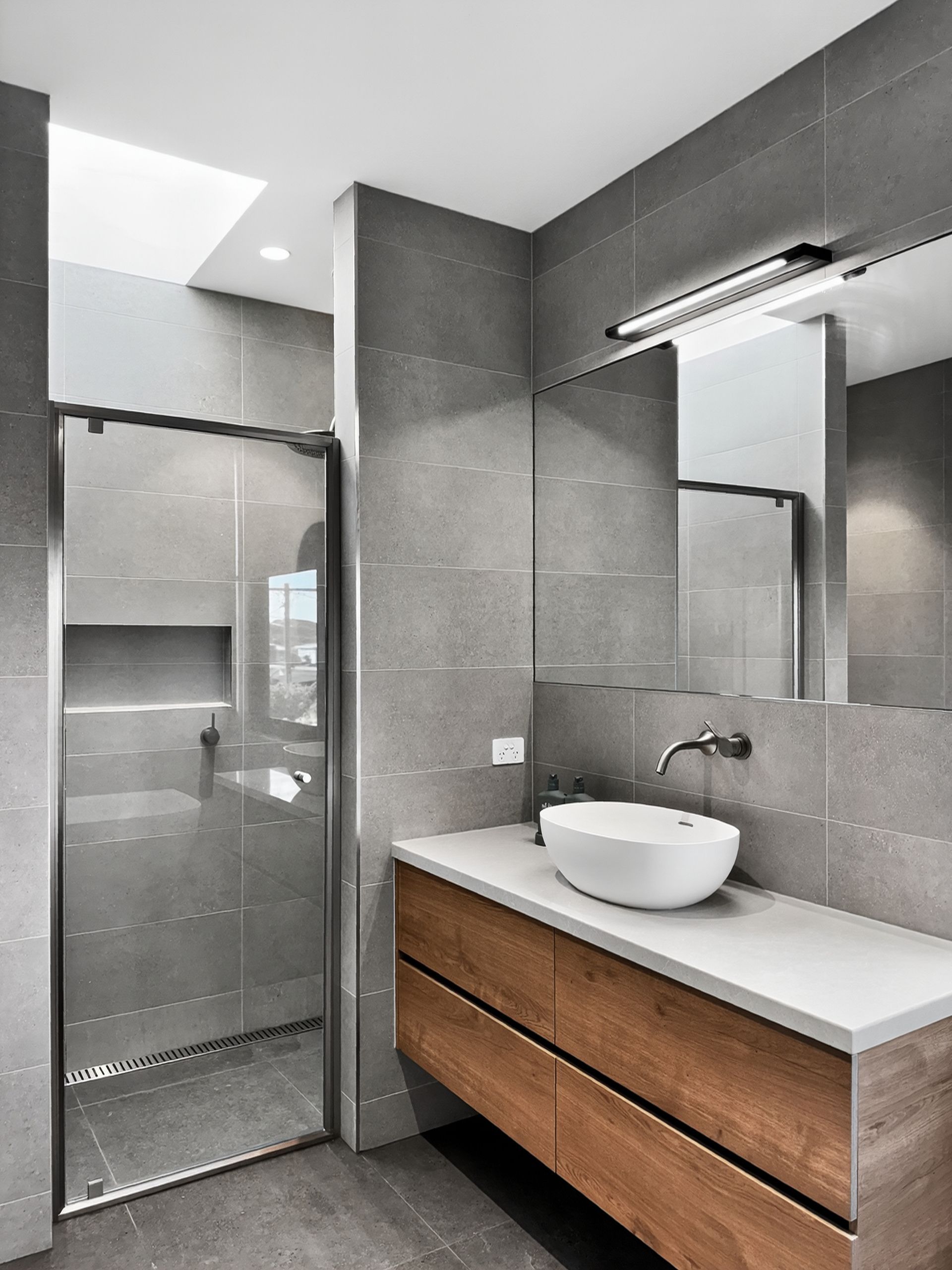 Modern bathroom with gray tiled walls, a wooden vanity, and a glass shower.