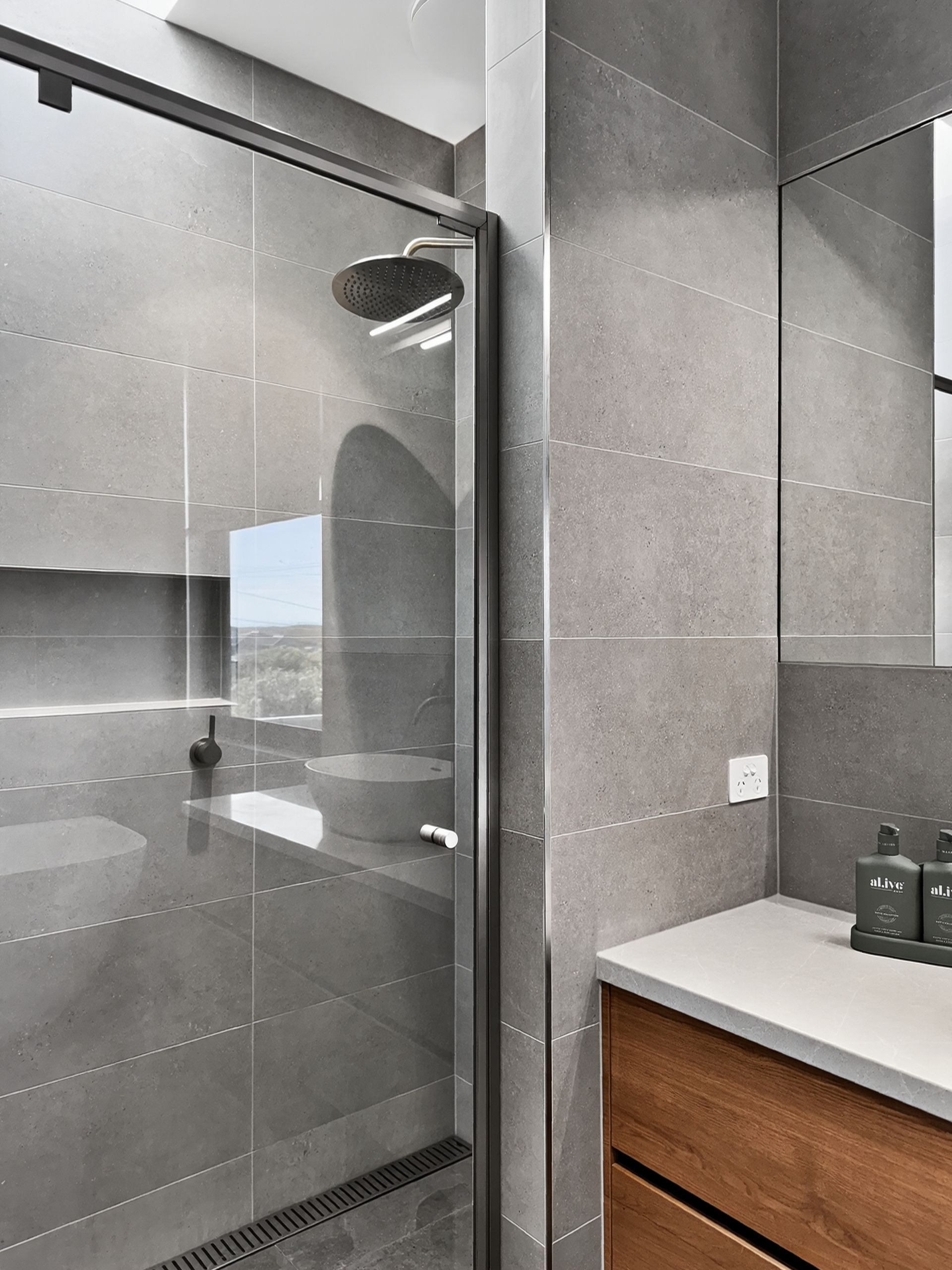 Gray-tiled bathroom with a glass shower door, wooden vanity, and large mirror.