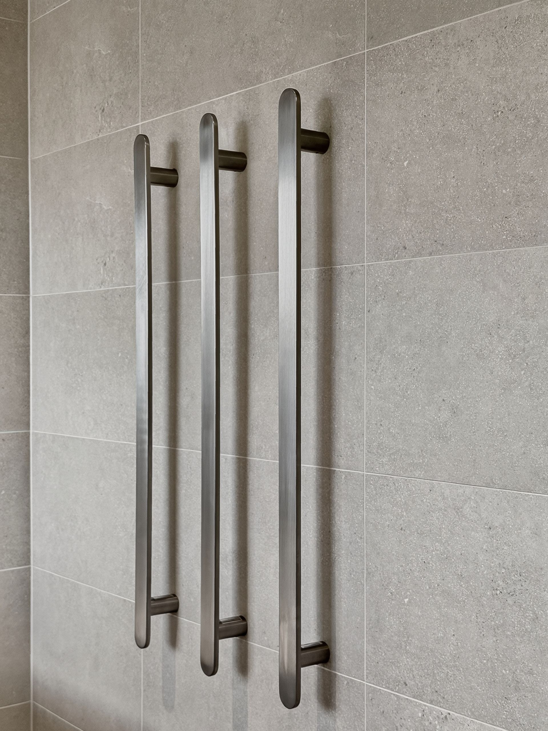 Three vertical towel warmers mounted on a gray tiled wall.