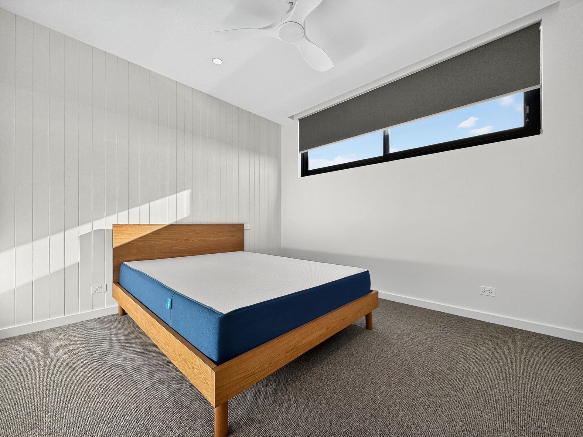 Bedroom with wooden bed frame, blue and white mattress, window with blinds.