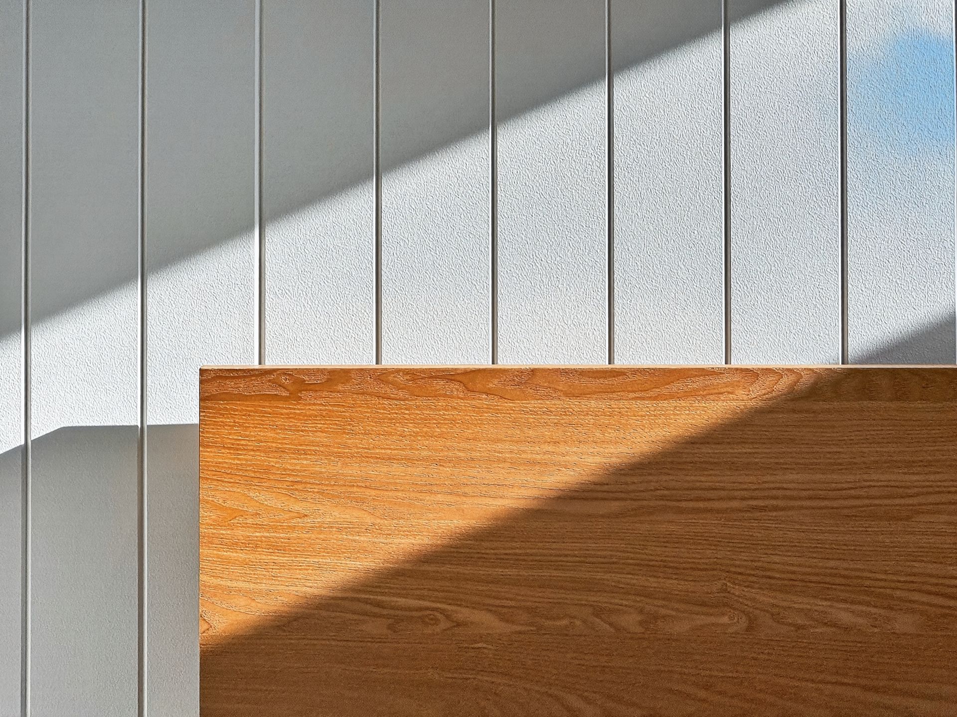 Wooden panel with a shadow against a gray textured wall.