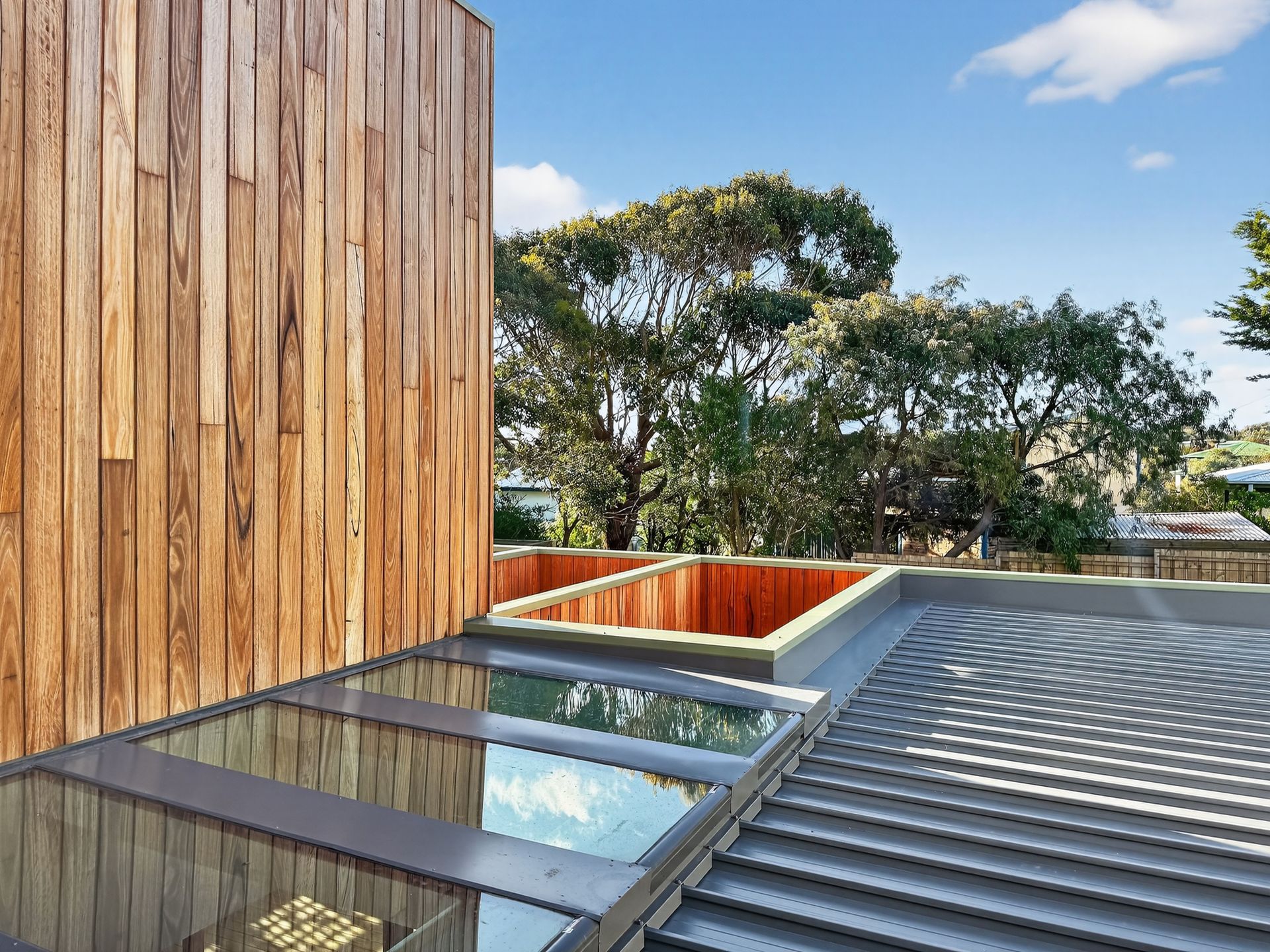 Exterior view of a modern building with wood siding, skylights, and a flat roof.