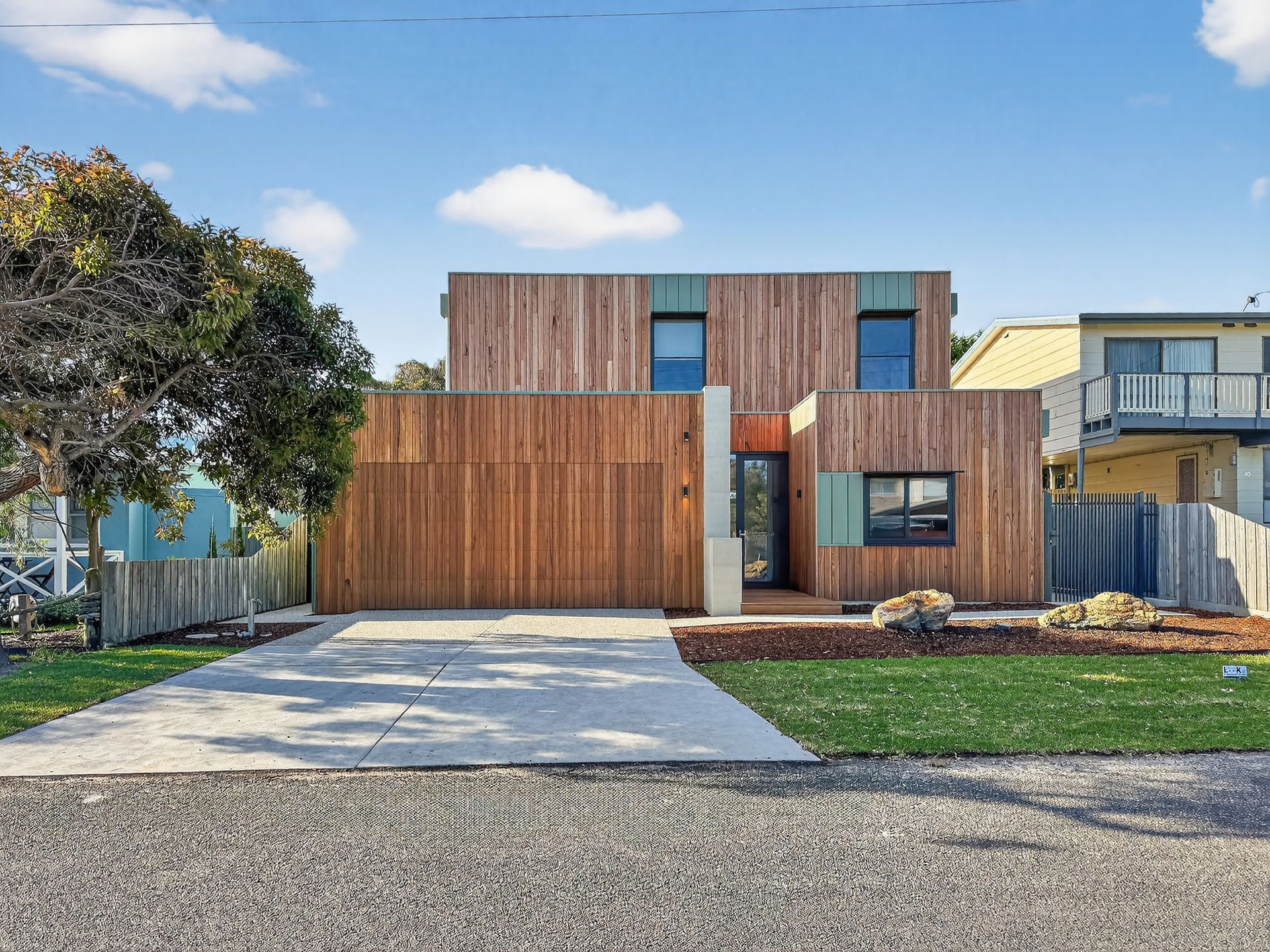 Modern two-story wooden house with a concrete driveway and small front yard. Cloudy sky above.
