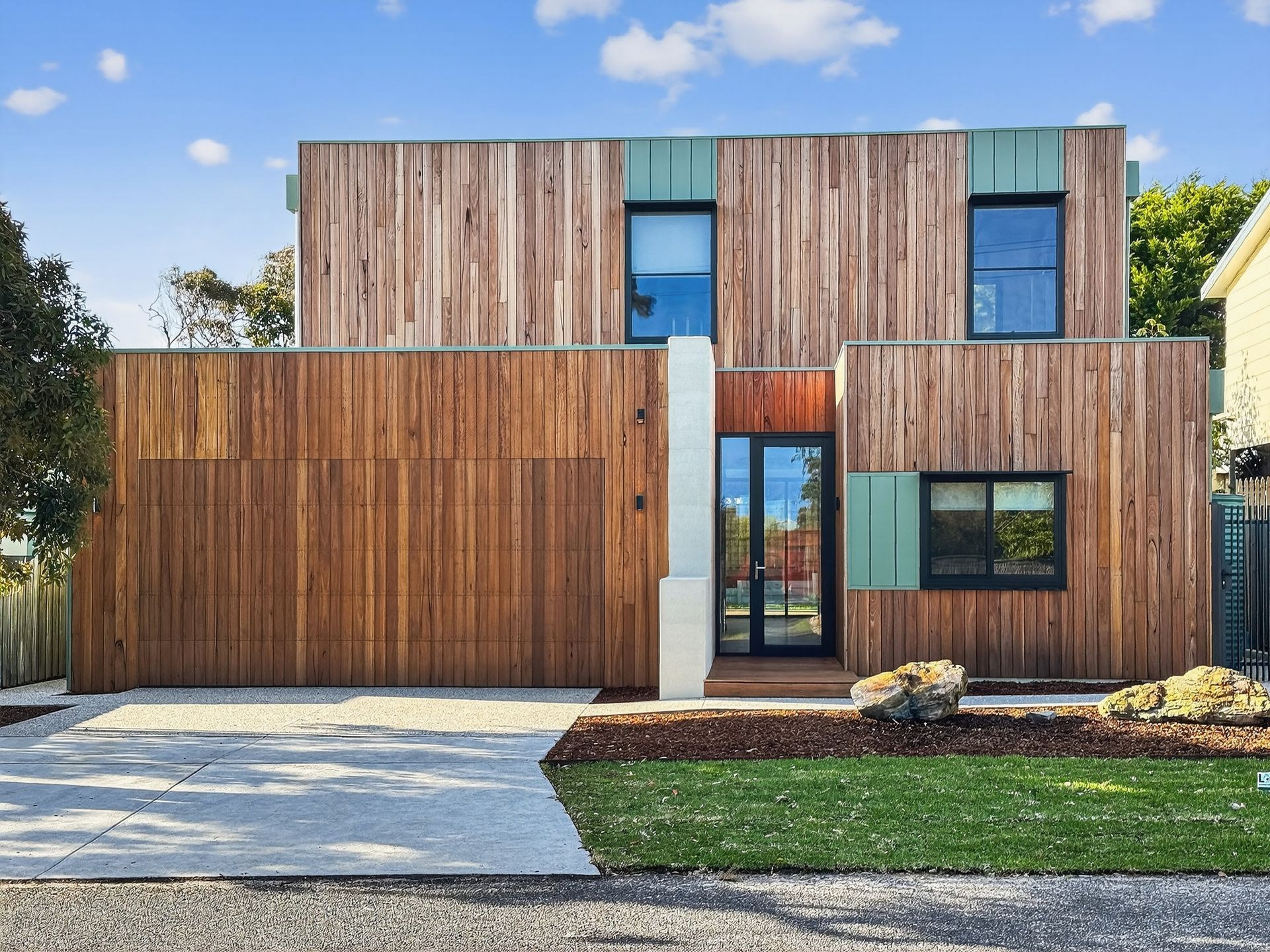 Modern two-story house with wood siding, a garage door, and black-framed windows; blue sky.