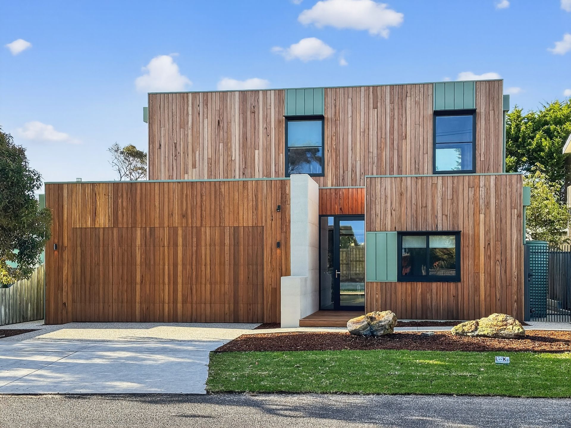 Modern two-story house with wood siding, a garage, small windows, and a manicured lawn.