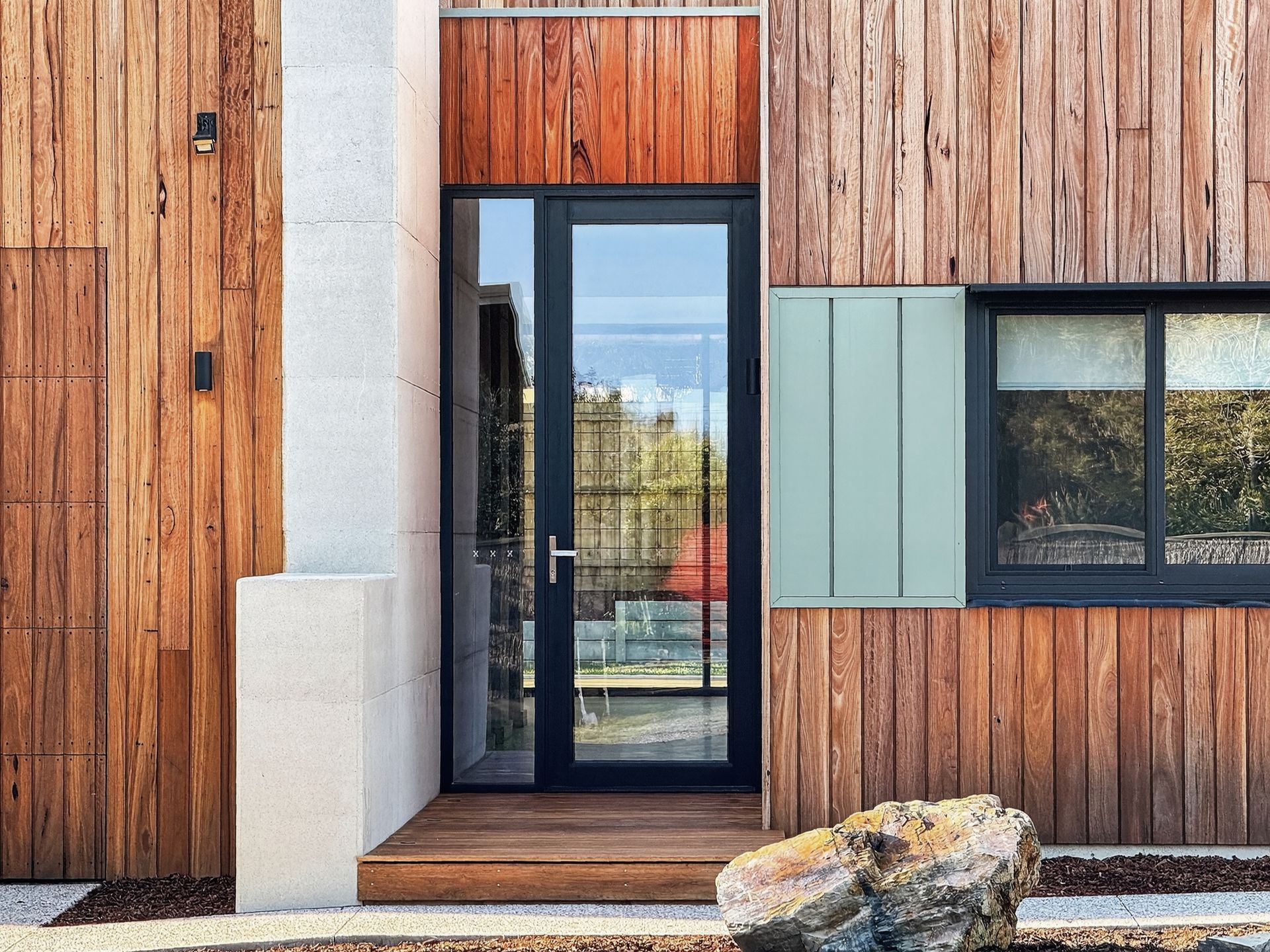 Wooden home entrance with glass door, small window, and stone accent.