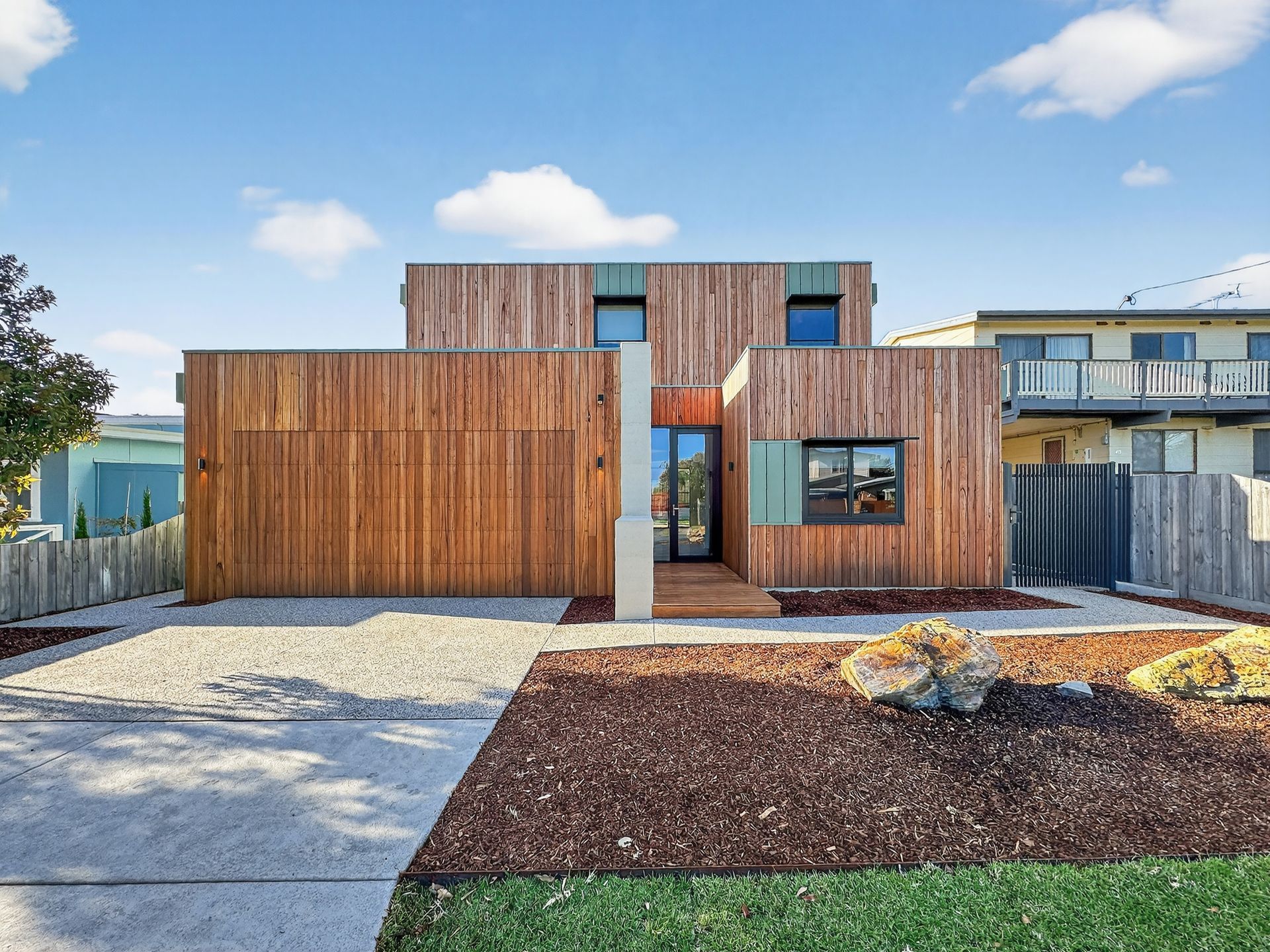Modern, wood-clad house with a gravel driveway, small front yard, and a cloudy sky.