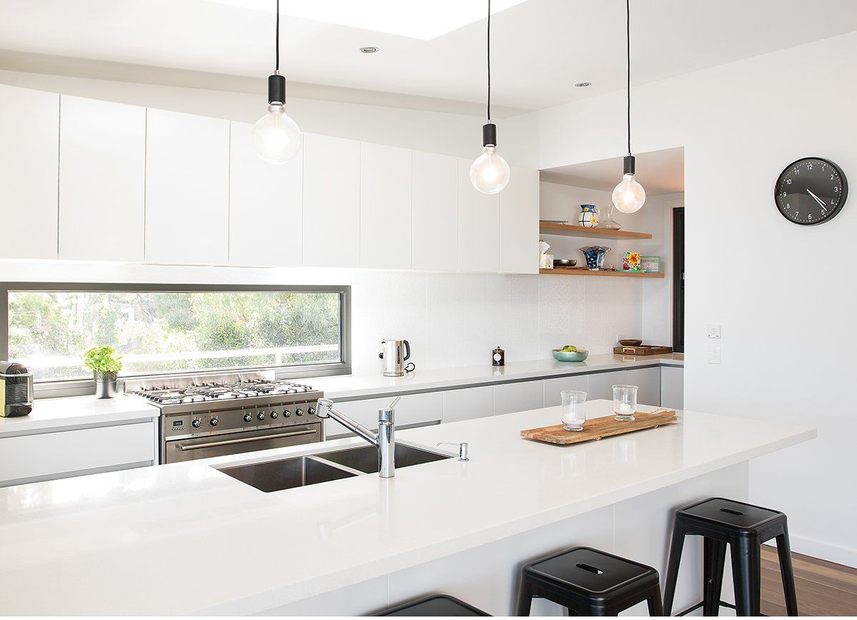 A kitchen with white cabinets , a sink , a stove and a window.