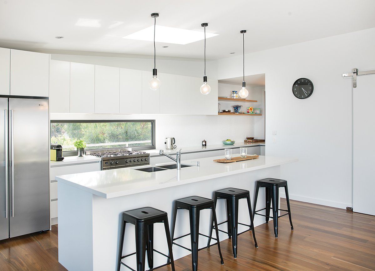 A kitchen with white cabinets , stools , a refrigerator , and a large island.
