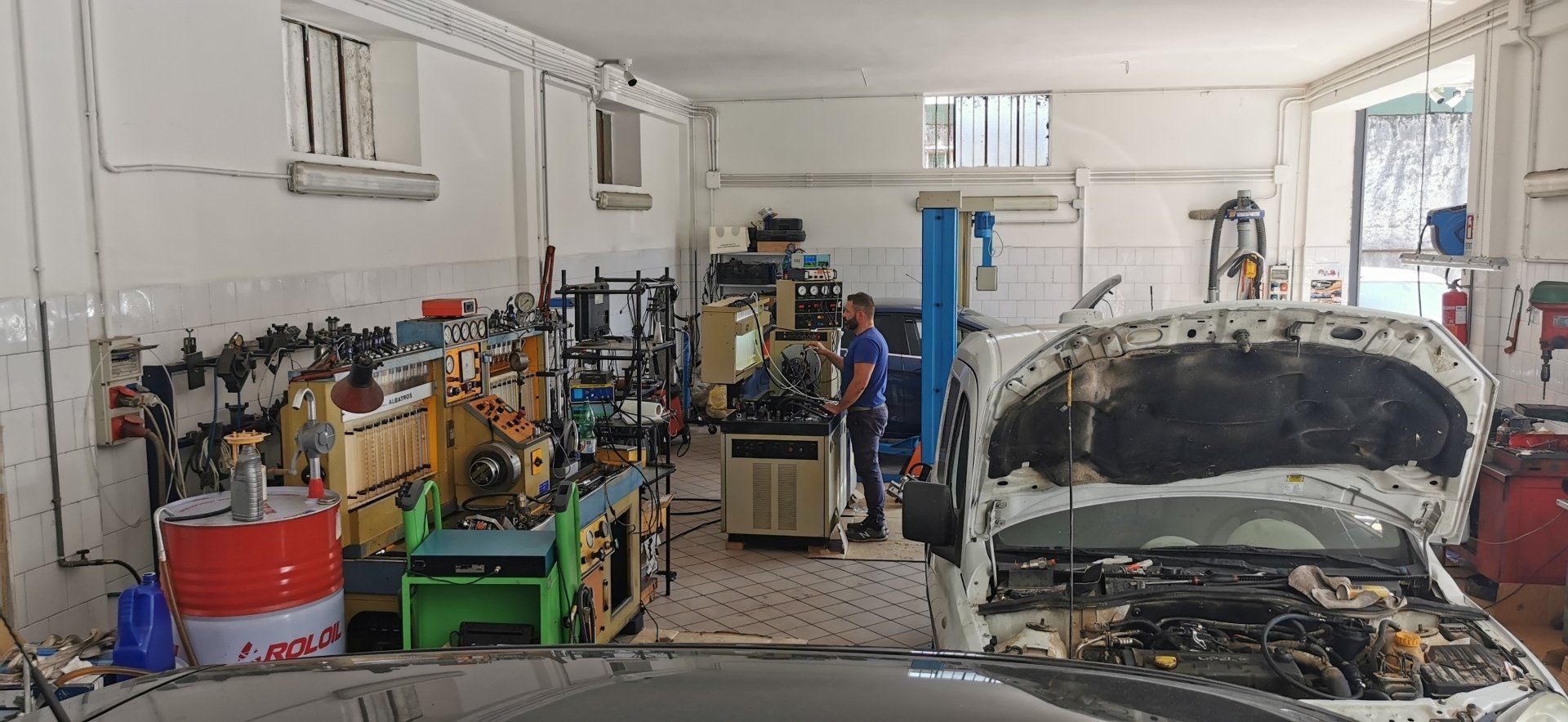 Interno di un'officina meccanica; un meccanico lavora su un'auto con il cofano aperto.