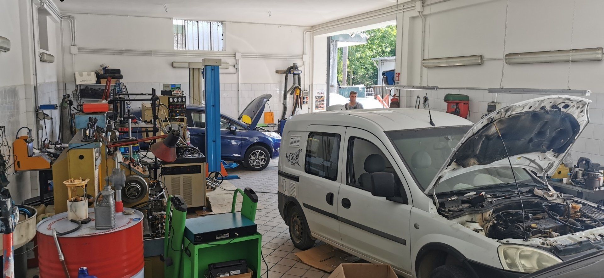 Un'officina con due auto in riparazione. Una è un furgone bianco e l'altra è una berlina blu.