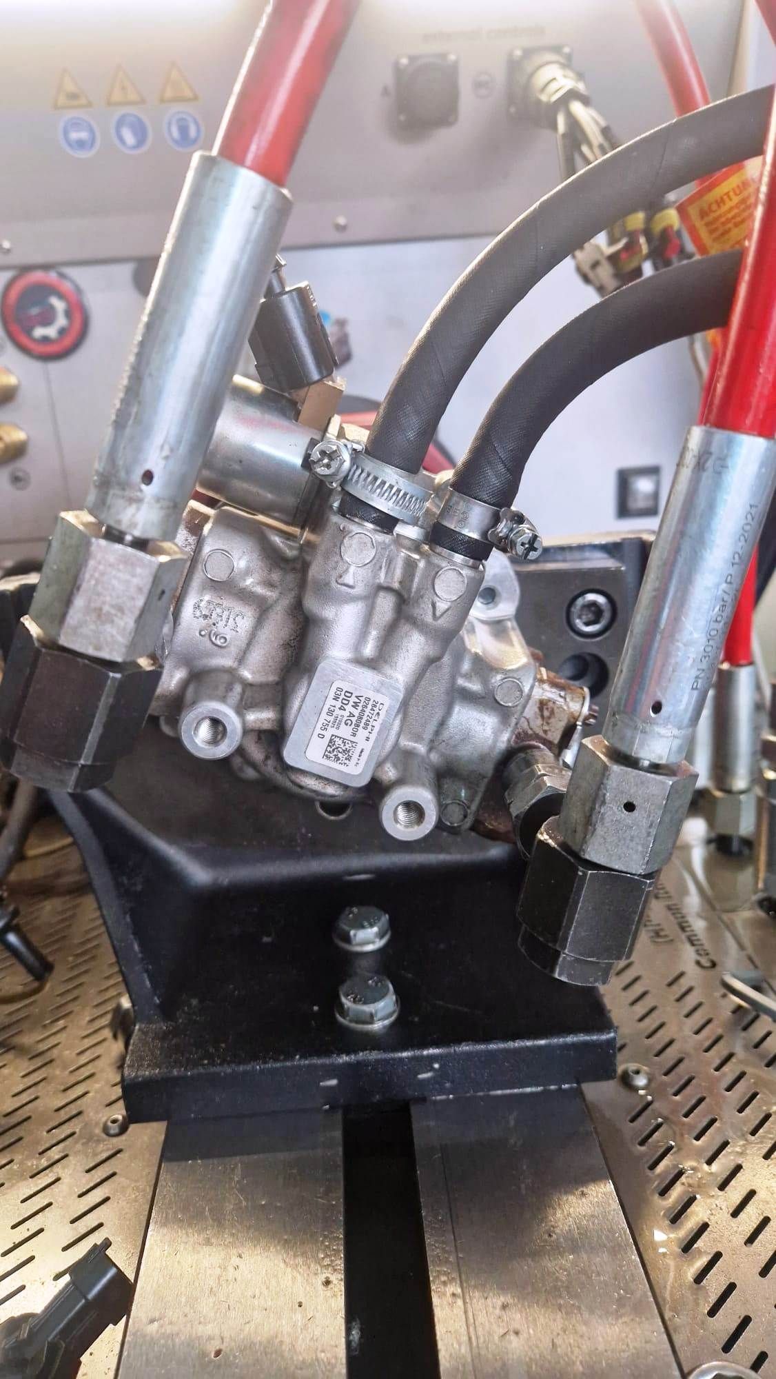 Primo piano di una pompa idraulica argentata montata su una staffa nera con tubi rossi e neri.