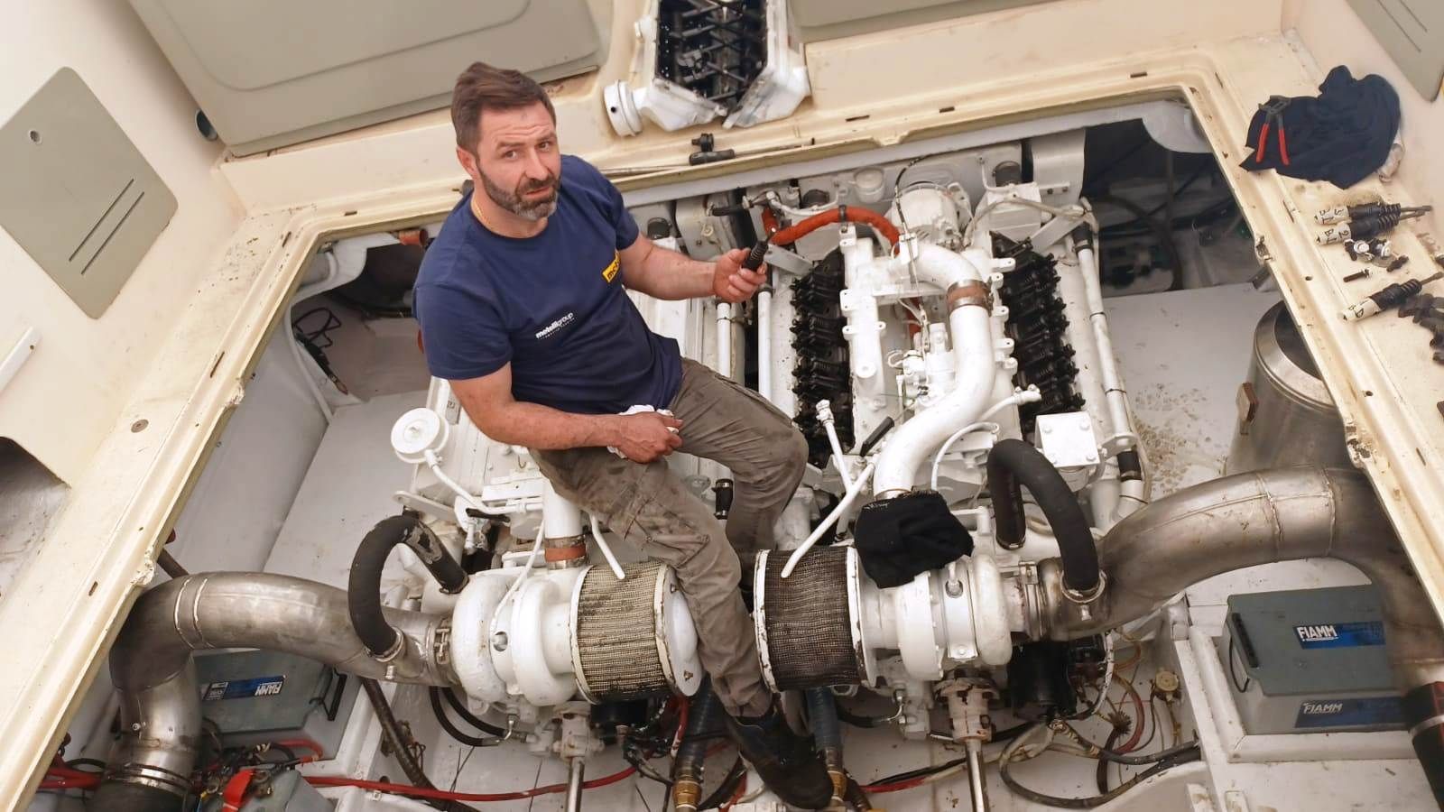 Un uomo nella sala macchine di una barca indica i motori bianchi.