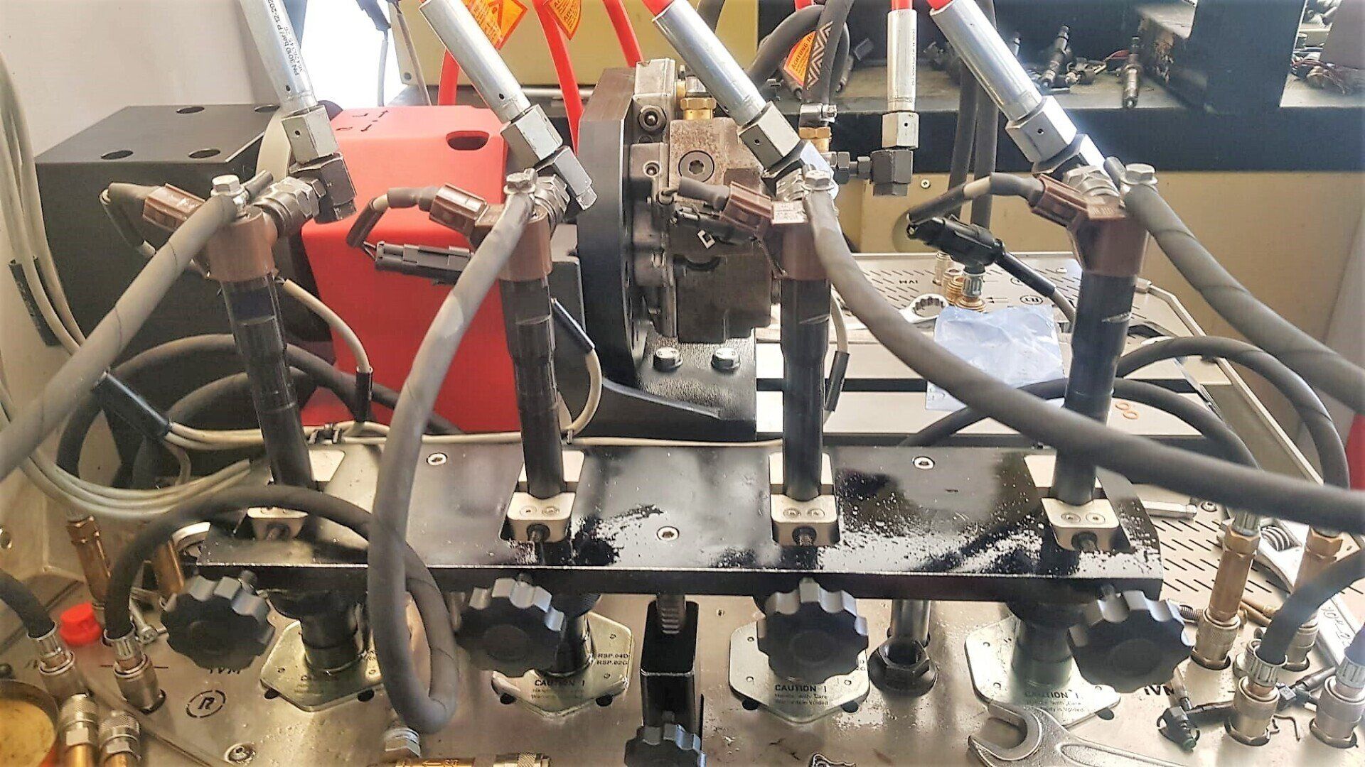 Iniettori del motore, tubi del carburante e componenti associati su un banco di prova, con un riquadro rosso sullo sfondo.