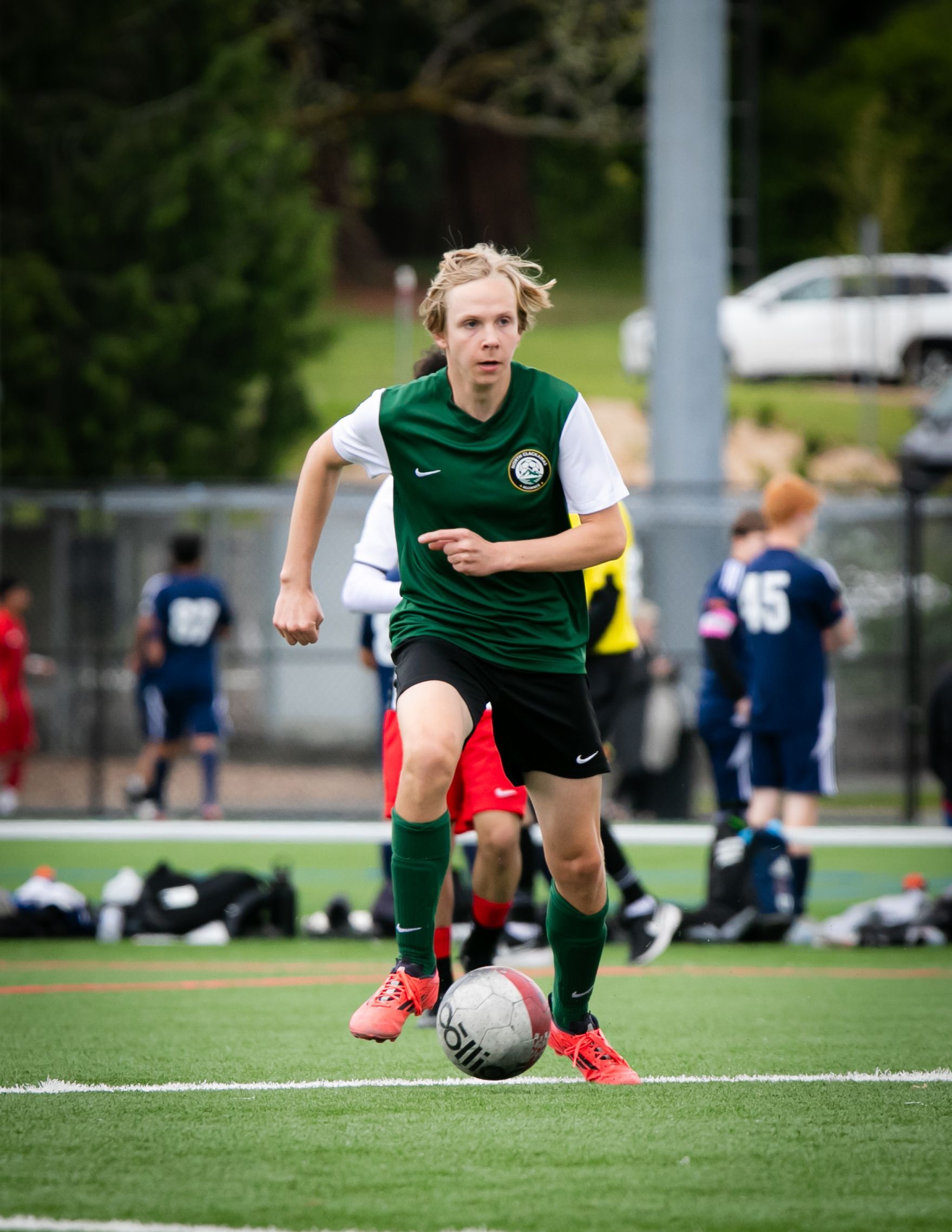 Soccer player in green and white jersey dribbles ball on a turf field.