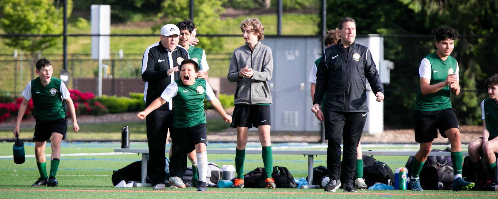 Soccer team on the sidelines celebrating; coach and players wearing green and black.
