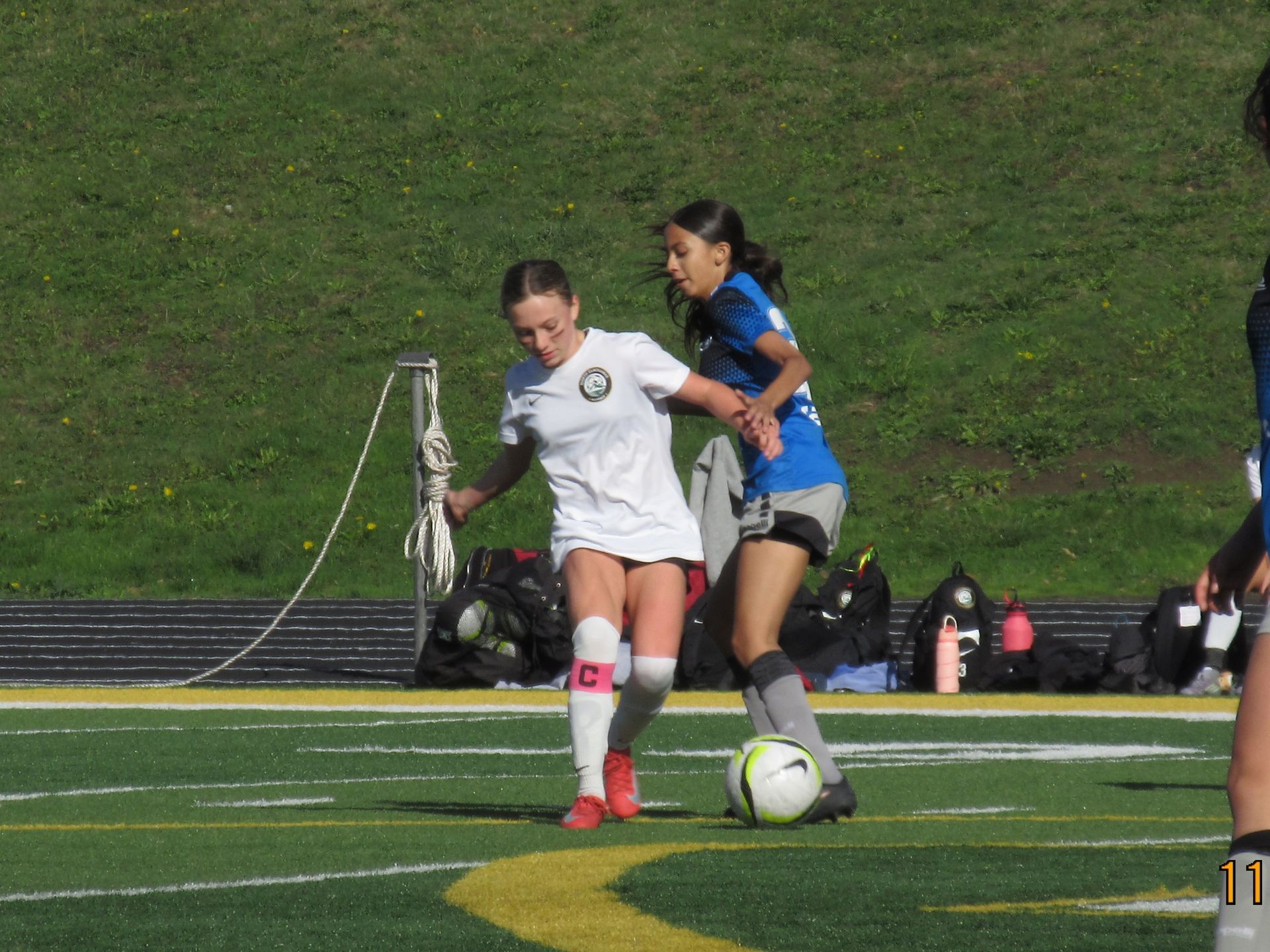 Two soccer players on a green field; one in white, the other in blue, both focused on the ball.