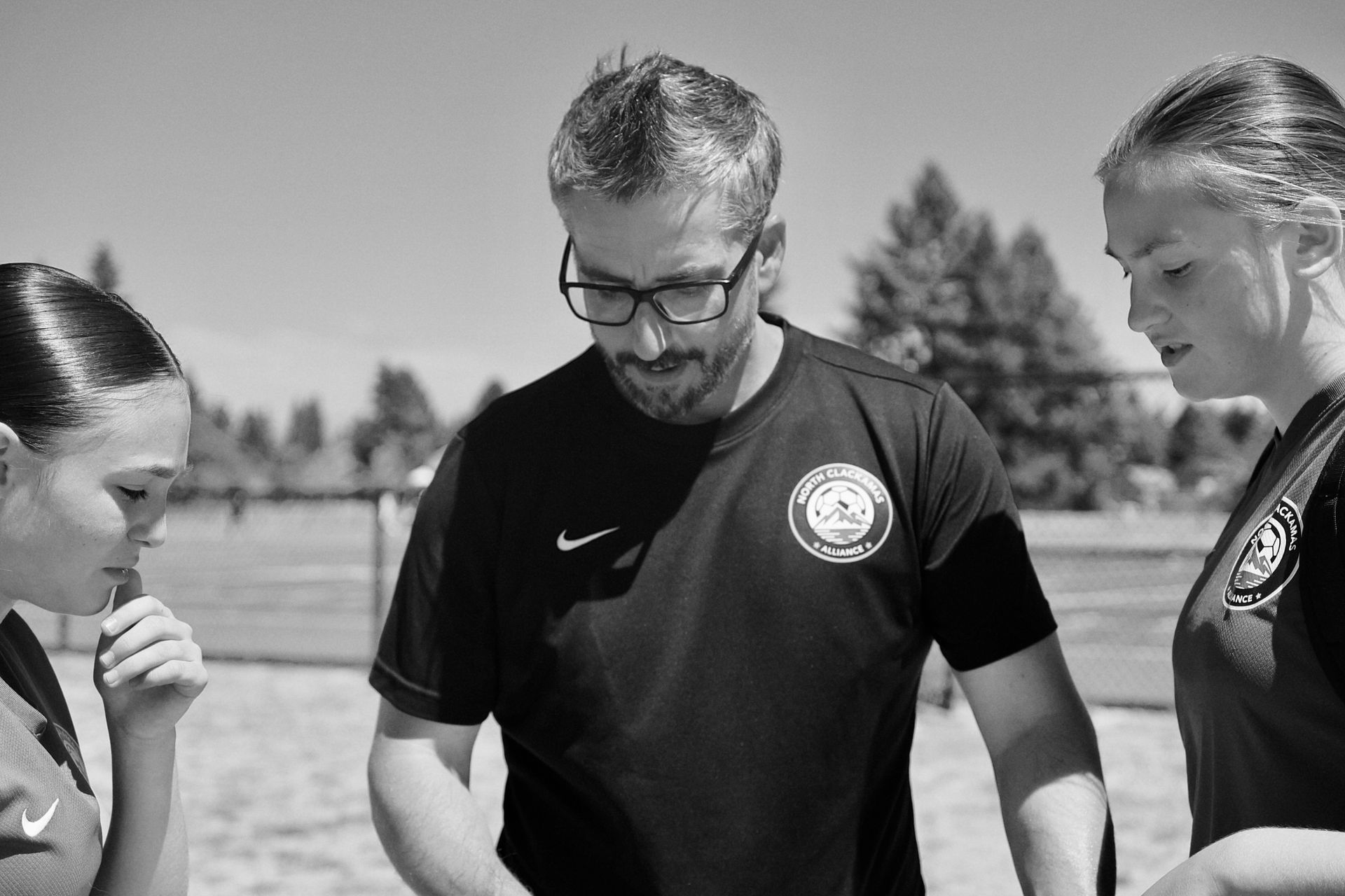 Coach talking to two soccer players on a field. They are looking down, possibly discussing strategy.