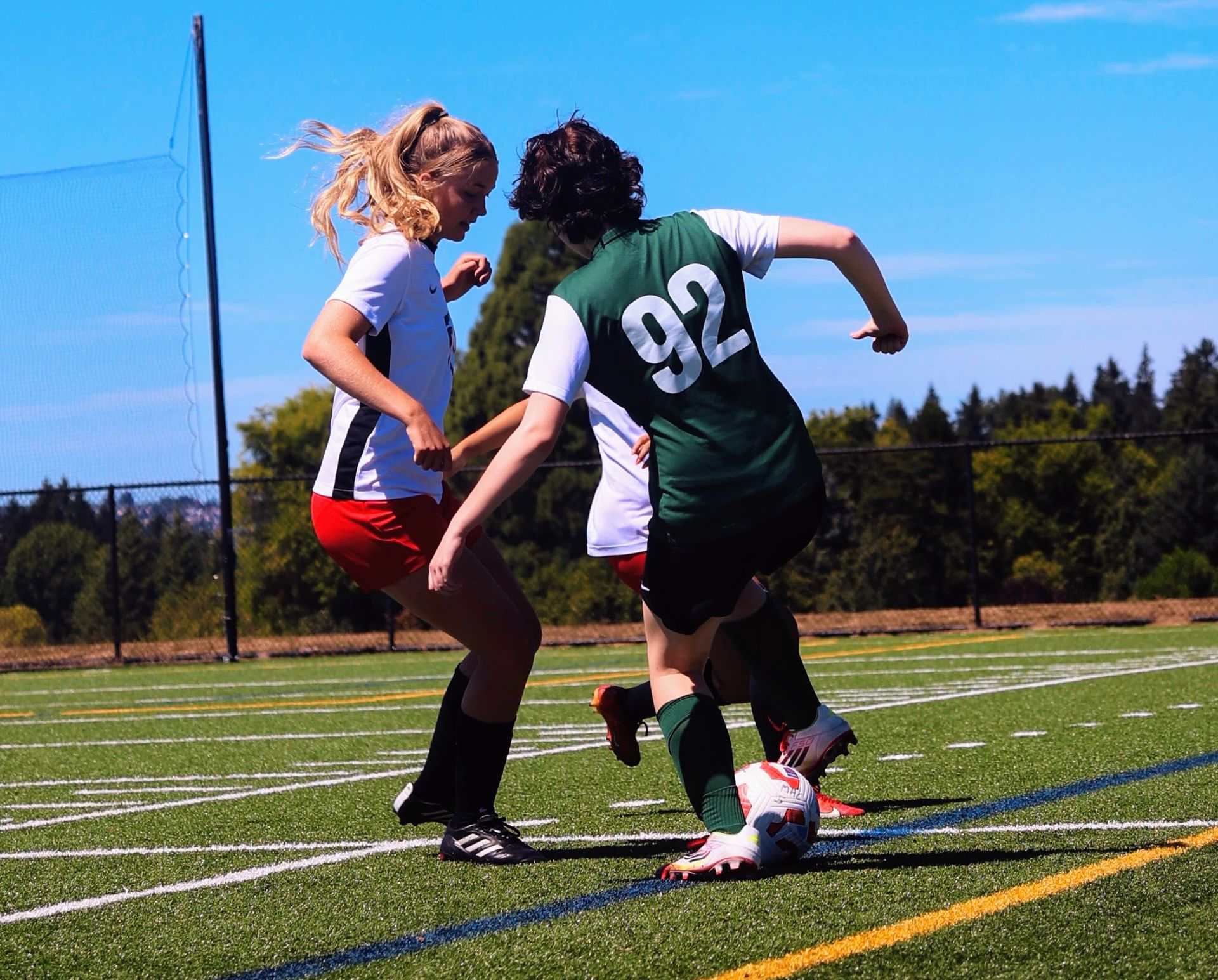 Two soccer players in a field, one in white and red, the other in green, competing for the ball.