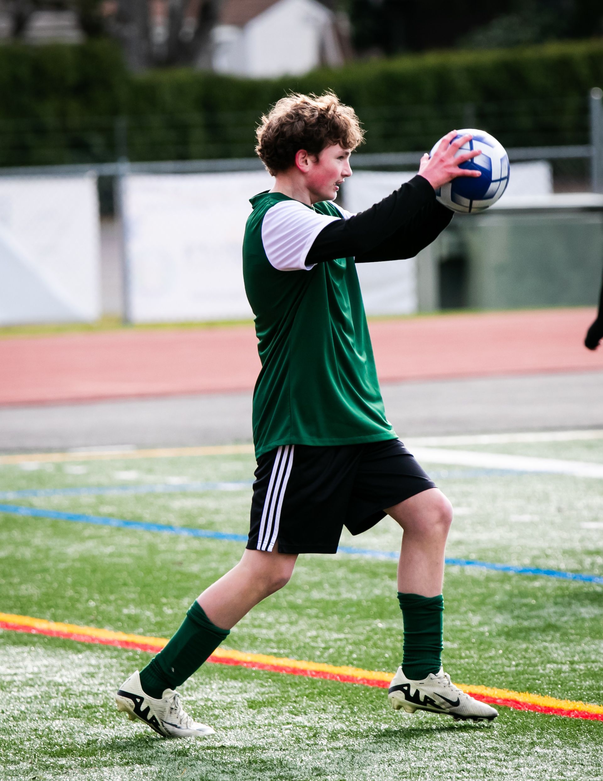 Soccer player in green jersey about to throw the ball during a game.