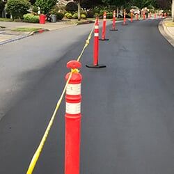 Freshly paved street blocked off with orange bollards and caution tape.