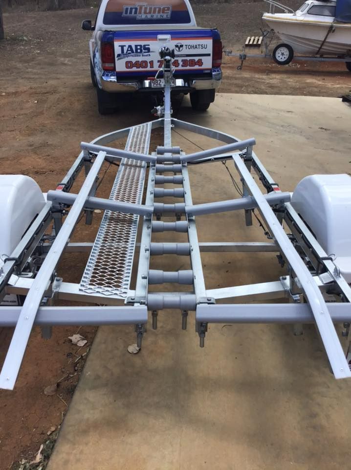 Boat Trailer With White Fenders And A Truck In The Background, Parked On Concrete — In Tune Marine in Mackay, QLD
