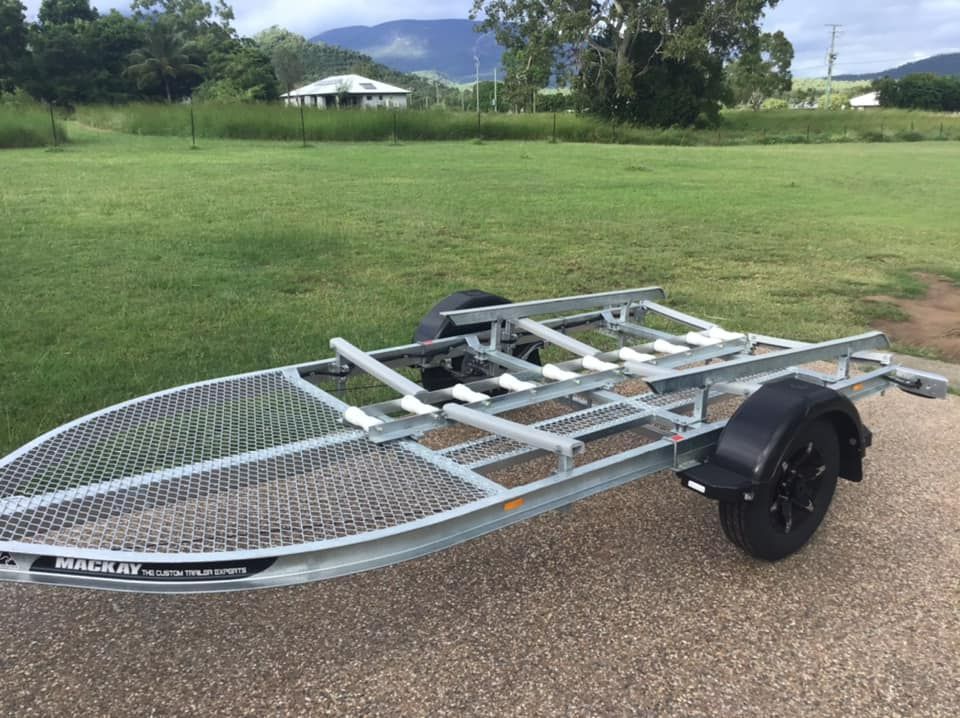 A Silver Boat Trailer On A Paved Surface In A Grassy Area With A House And Mountains In The Background — In Tune Marine in Mackay, QLD