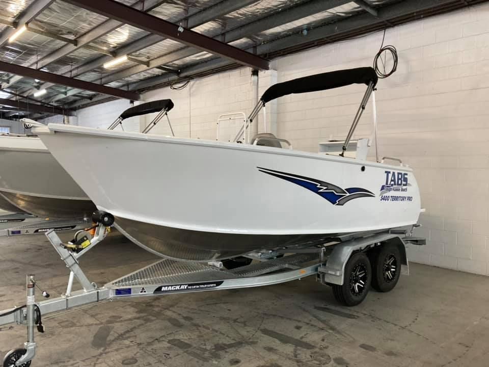 White Boat On A Trailer, Inside A Warehouse. Boat Has A Black Canopy And Blue Logo — In Tune Marine in Mackay, QLD