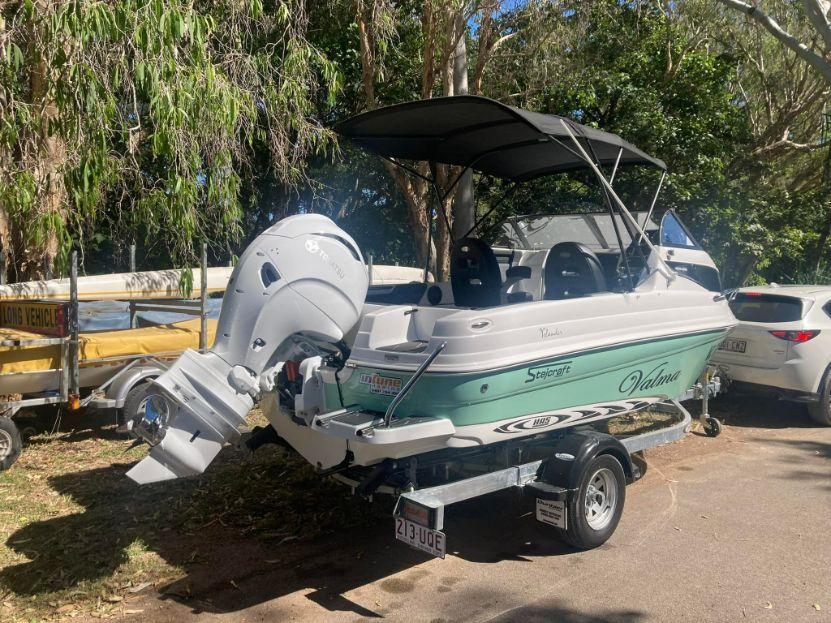 Boat On A Trailer, White And Teal With A Black Canopy, Parked On Pavement Near Trees — In Tune Marine in Mackay, QLD